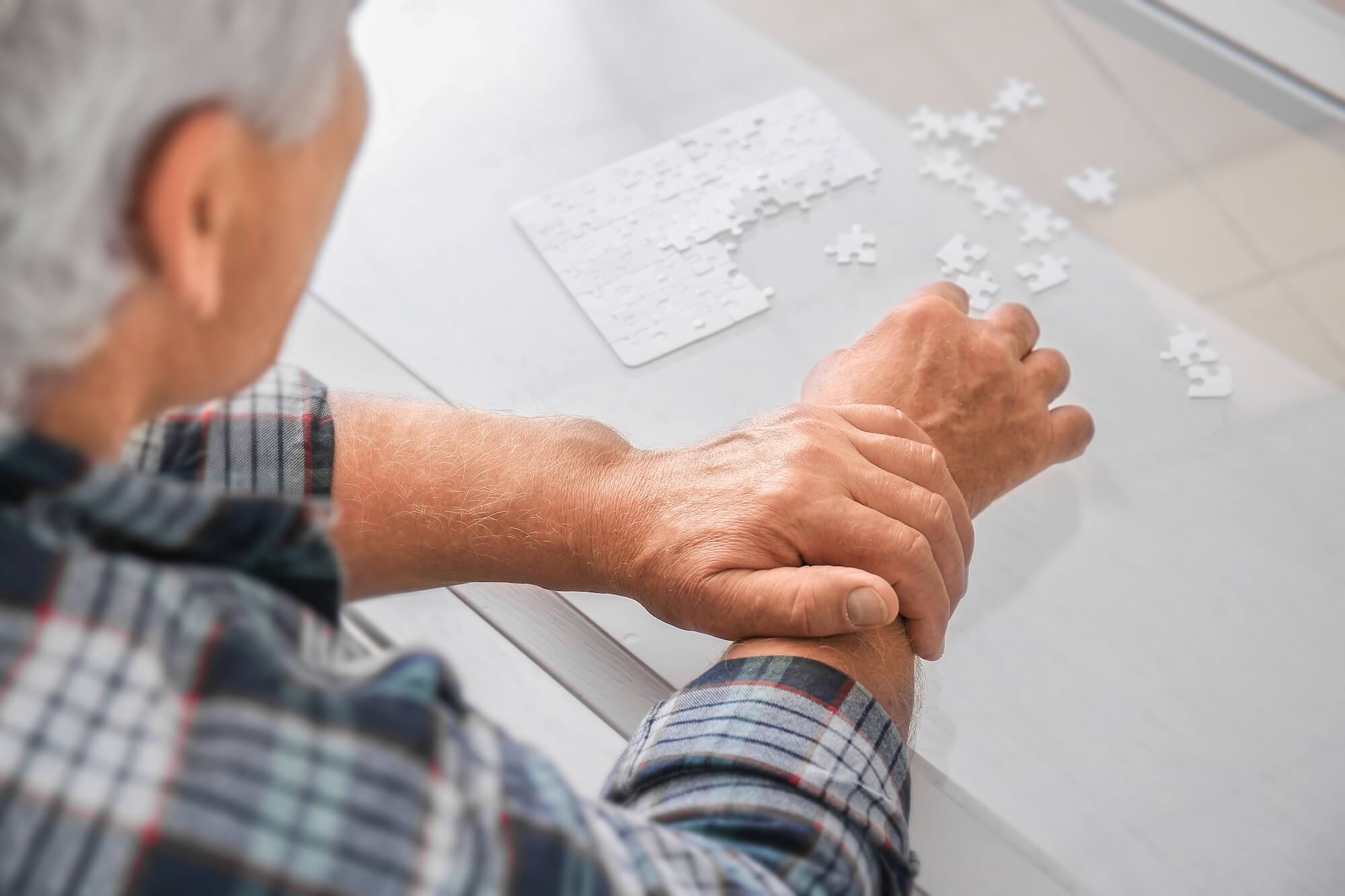 Alter Mann mit Parkinson hält mit der Hand seinen Arm fest