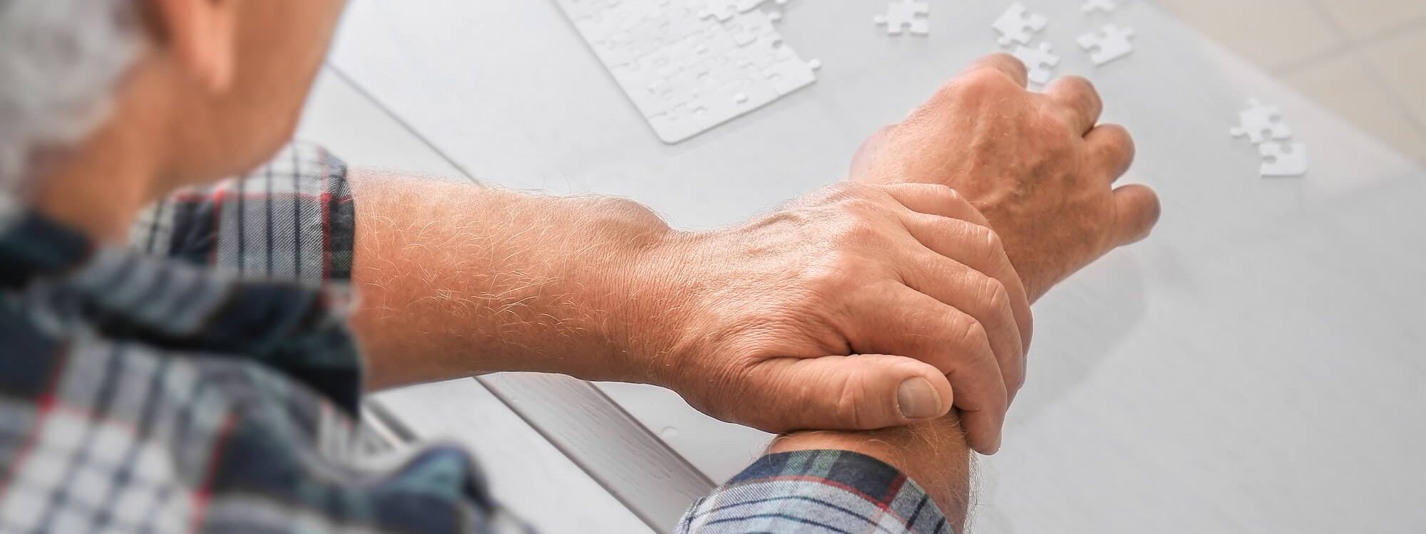 Alter Mann mit Parkinson hält mit der Hand seinen Arm fest