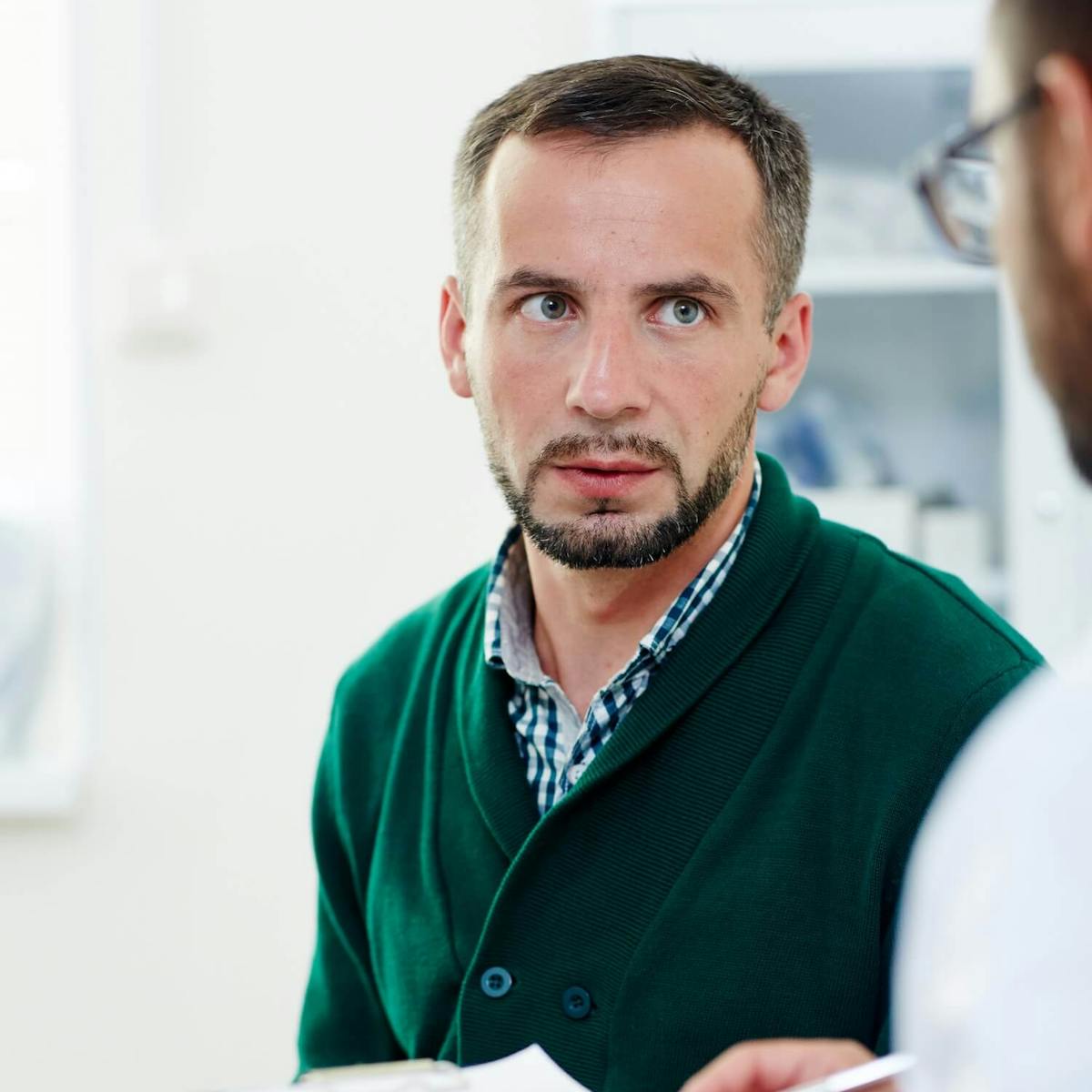 Kranker Patient sitzt im Behandlungszimmer und schaut den Arzt an