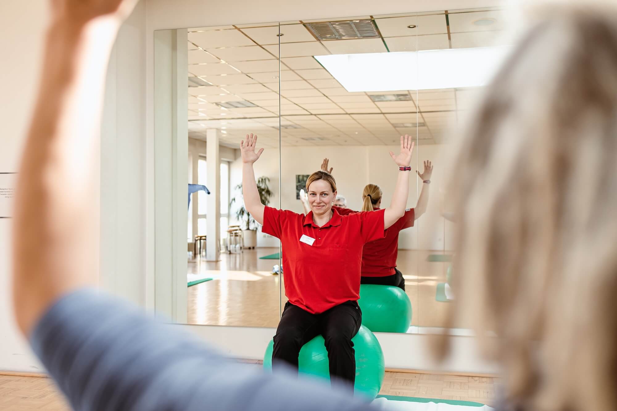 Physiotherapeutin sitzt auf einem Gymnastikball und hebt die Arme hoch