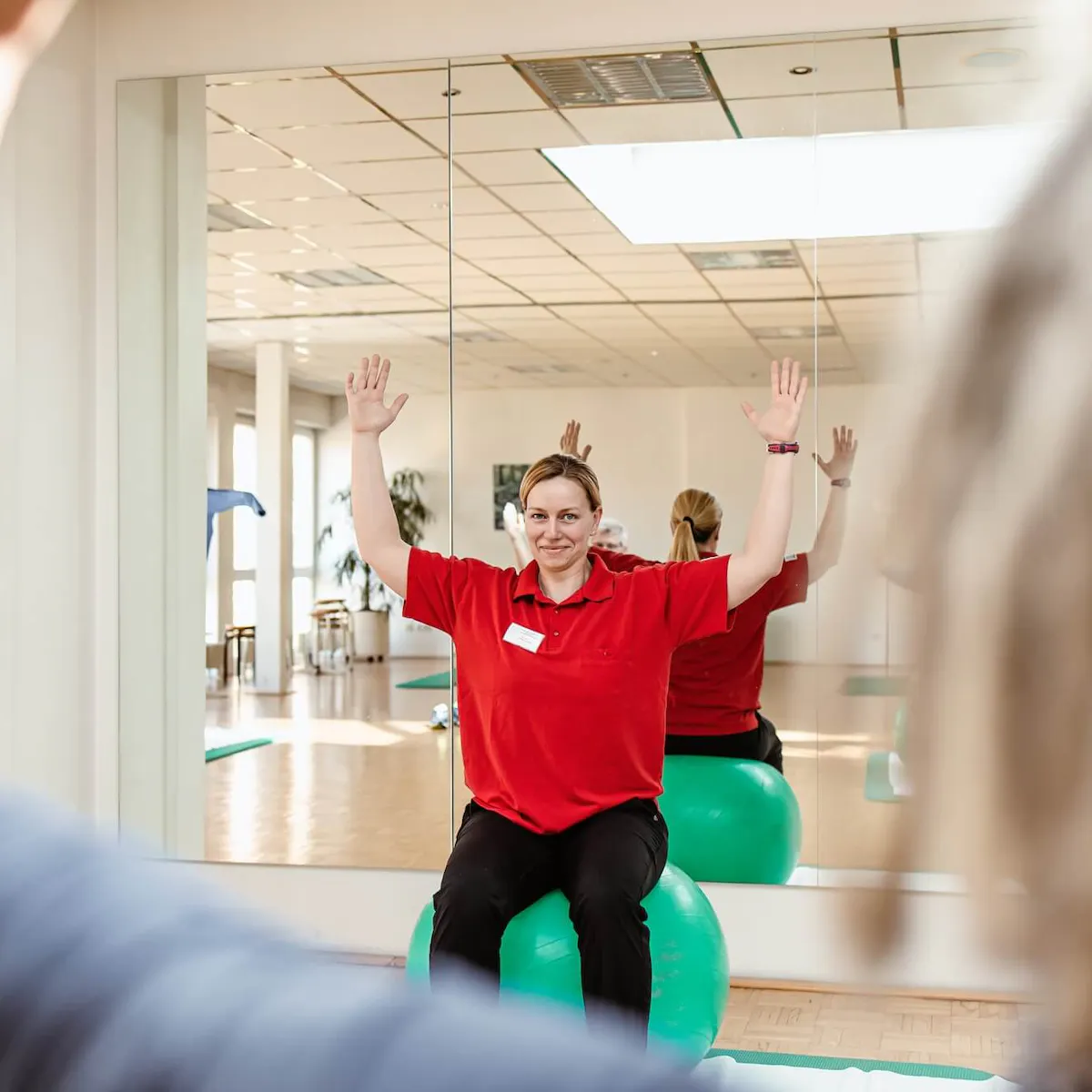 Bewegungstherapeutin macht Übung auf einem Gymnastikball vor