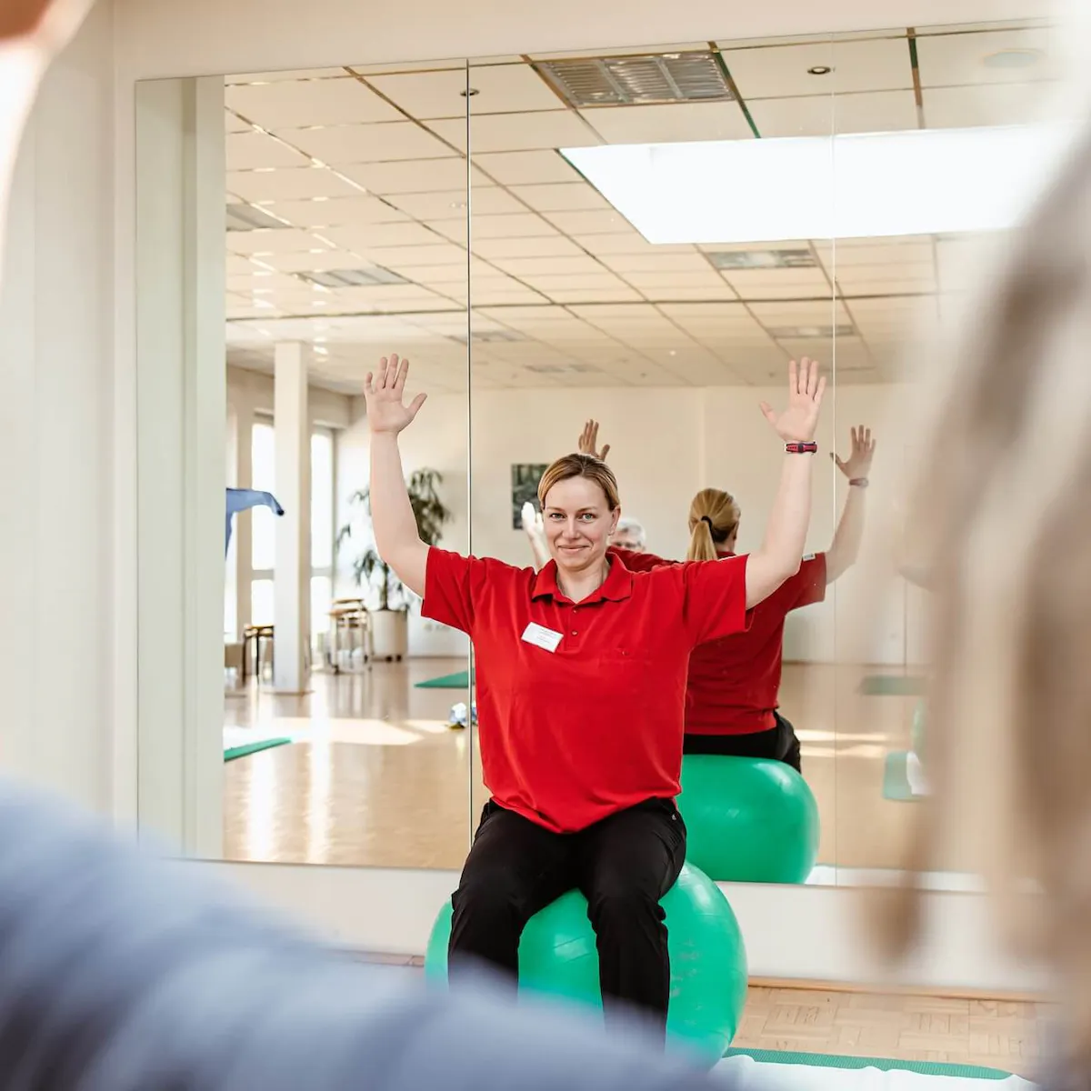 Physiotherpeutin der Reha Klinik macht Übung auf einem Gymnastikball vor