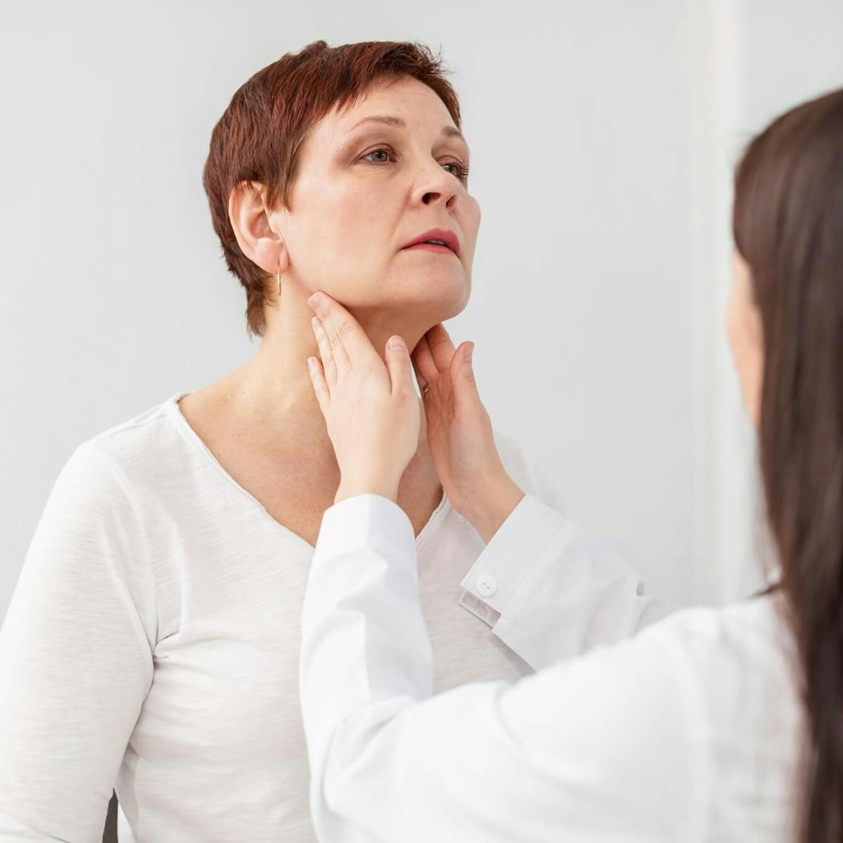 Ärztin tastet mit den Händen den Hals einer Patientin ab