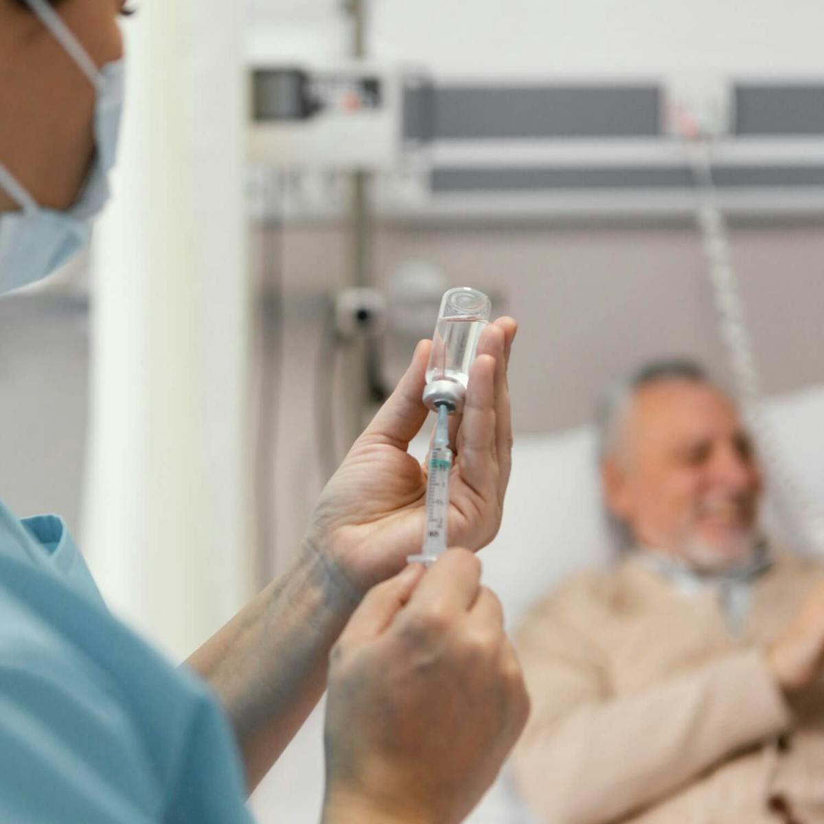 Pflegekraft zieht eine Spritze auf, während ein älterer Krebspatient im Krankenhausbett liegt