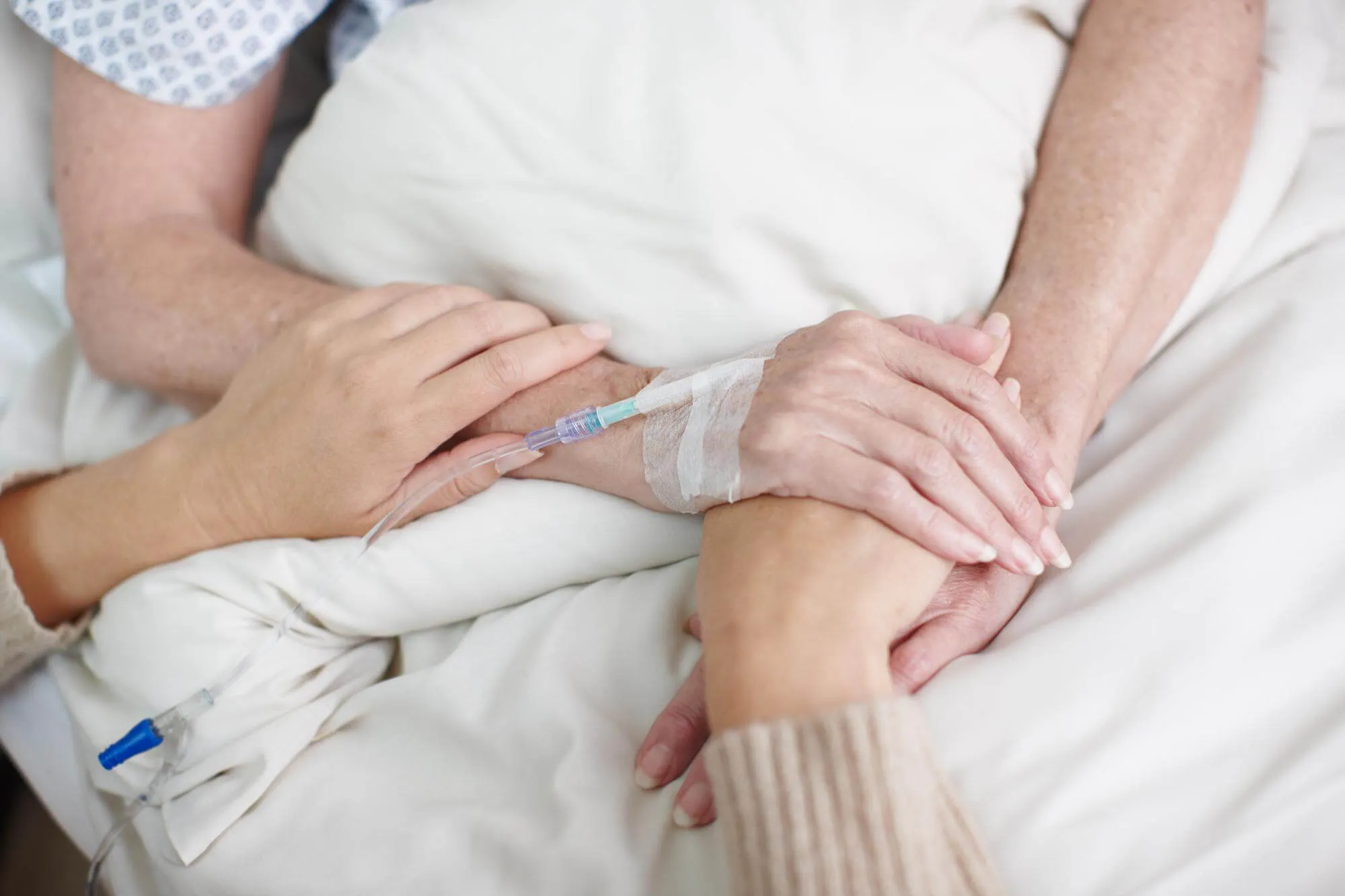 Angehörige hält die Hand einer Patientin am Krankenhausbett