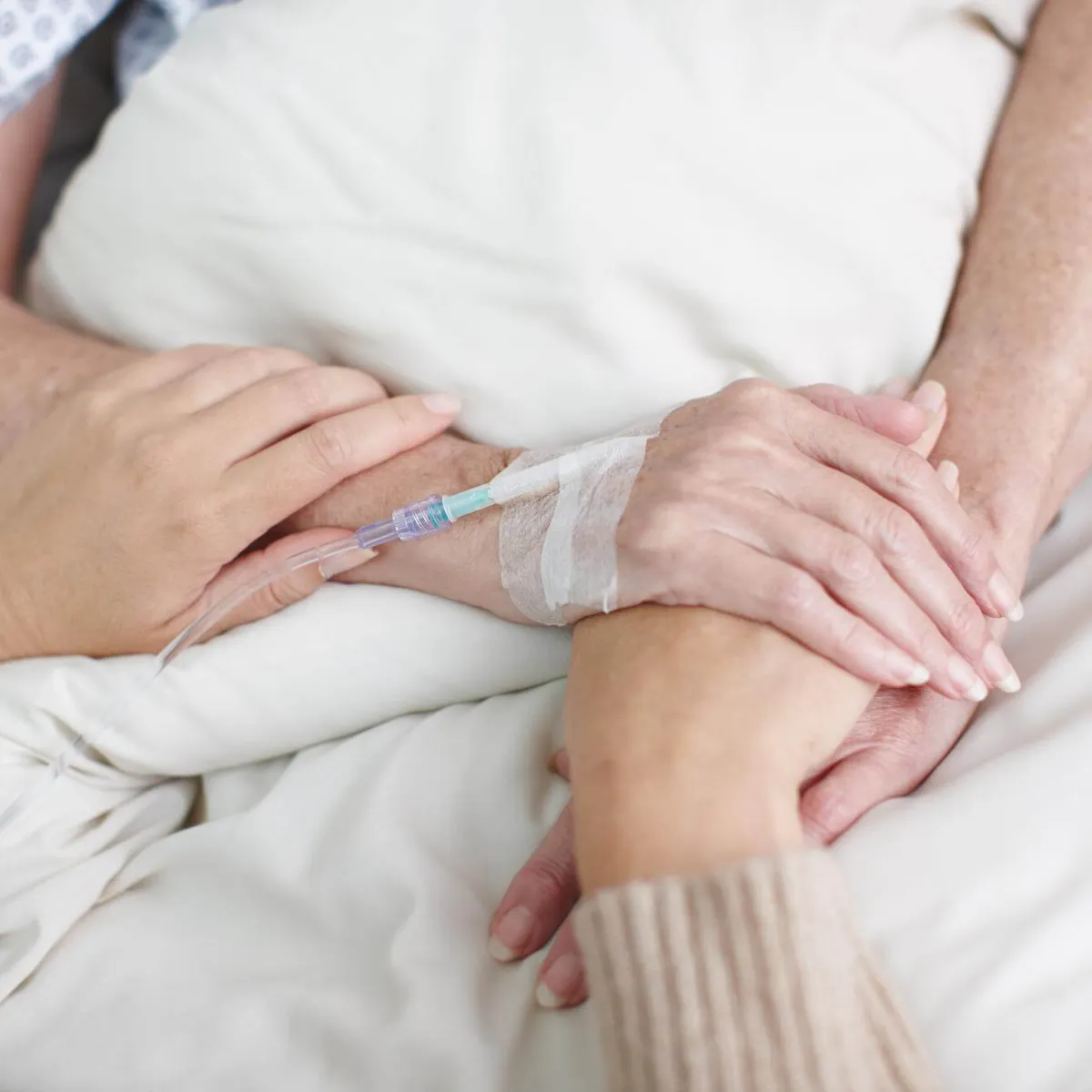 Angehörige hält die Hand einer Krebspatientin im Krankenhausbett