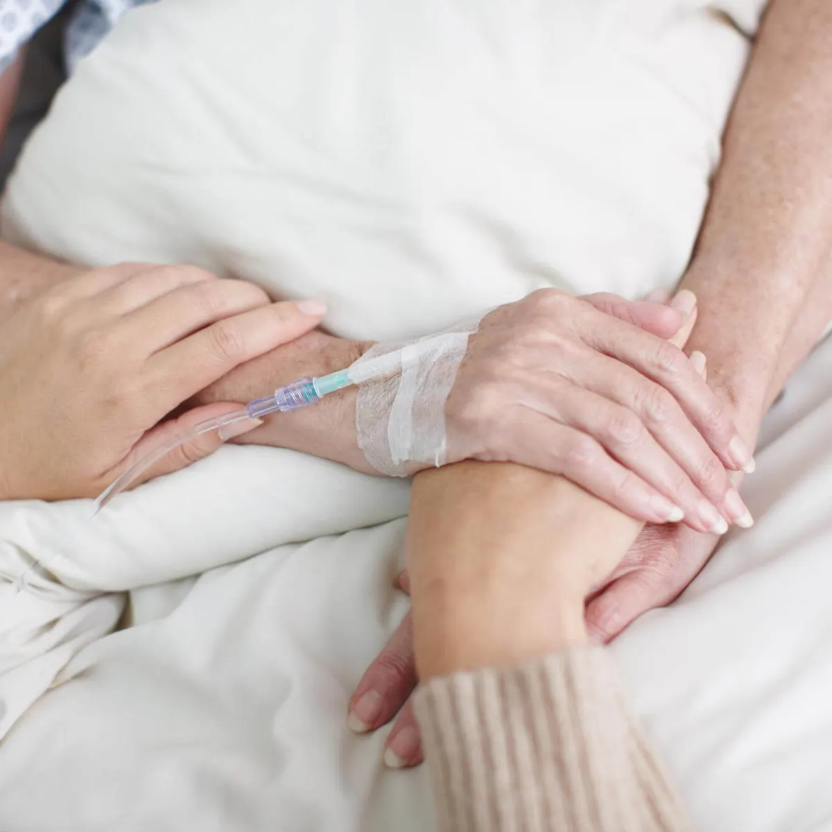 Angehörige hält die Hand einer Krebspatientin im Krankenhausbett
