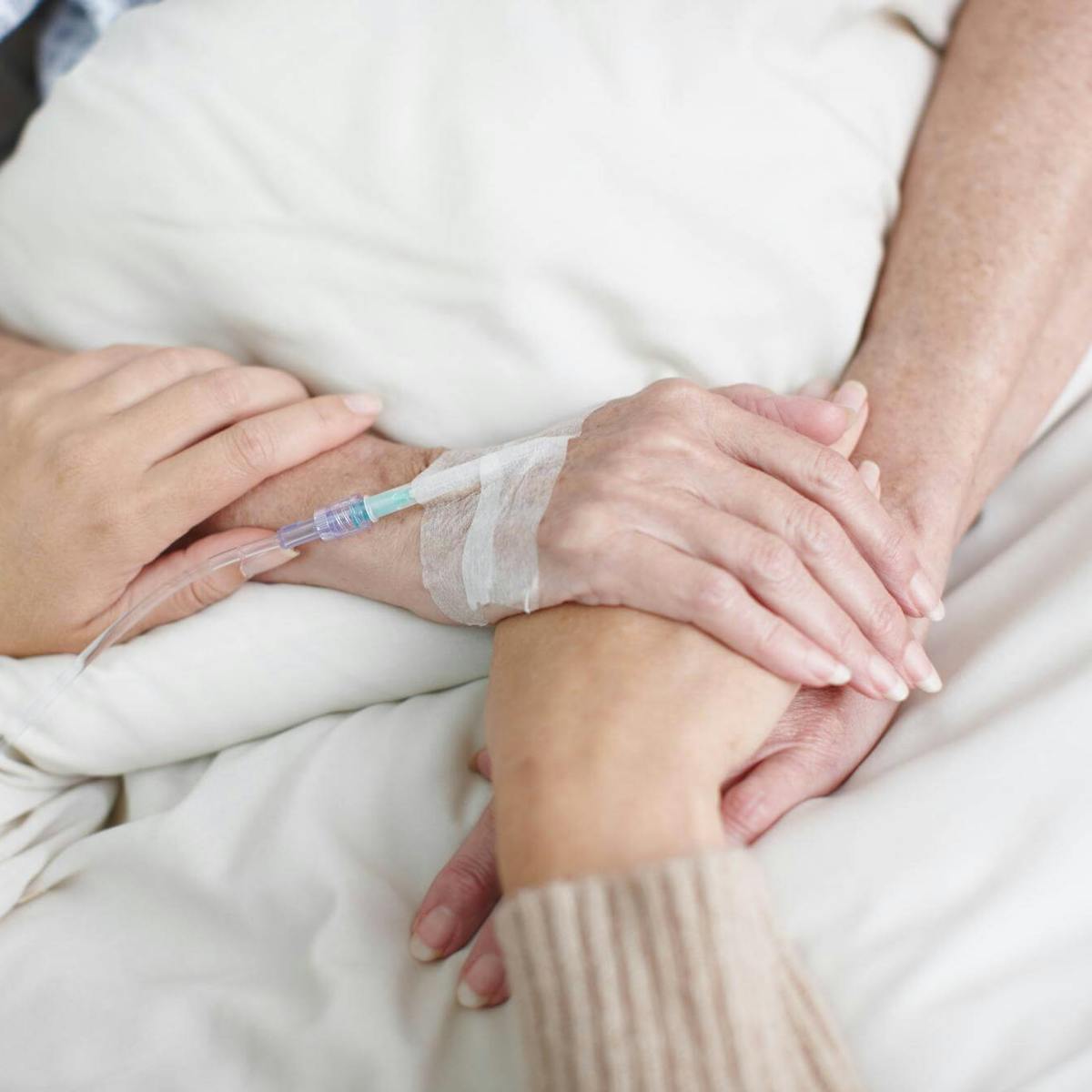 Angehörige hält Hand einer Patientin nach Operation am Krankenhausbett