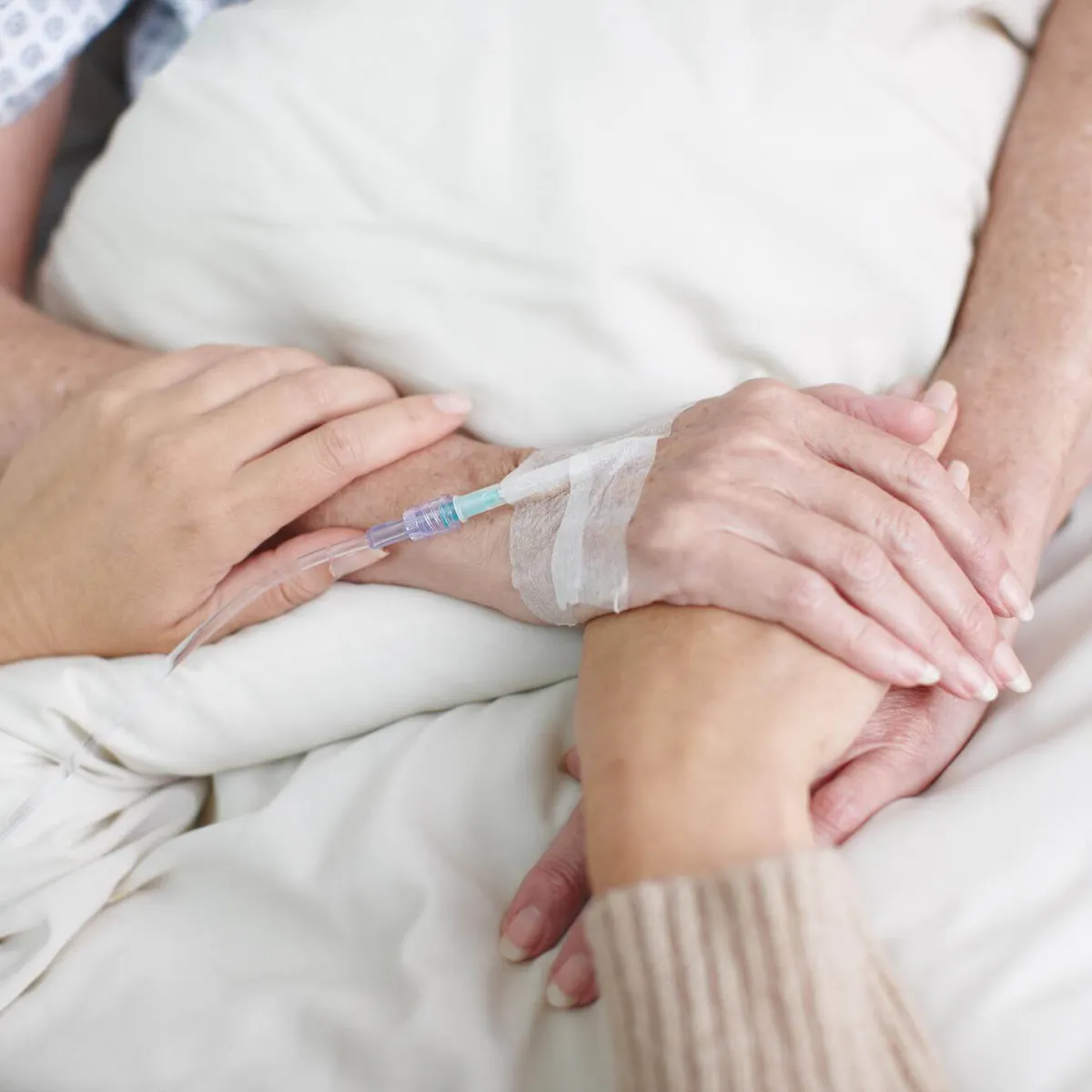 Angehörige und Patientin halten Hände am Krankenhausbett