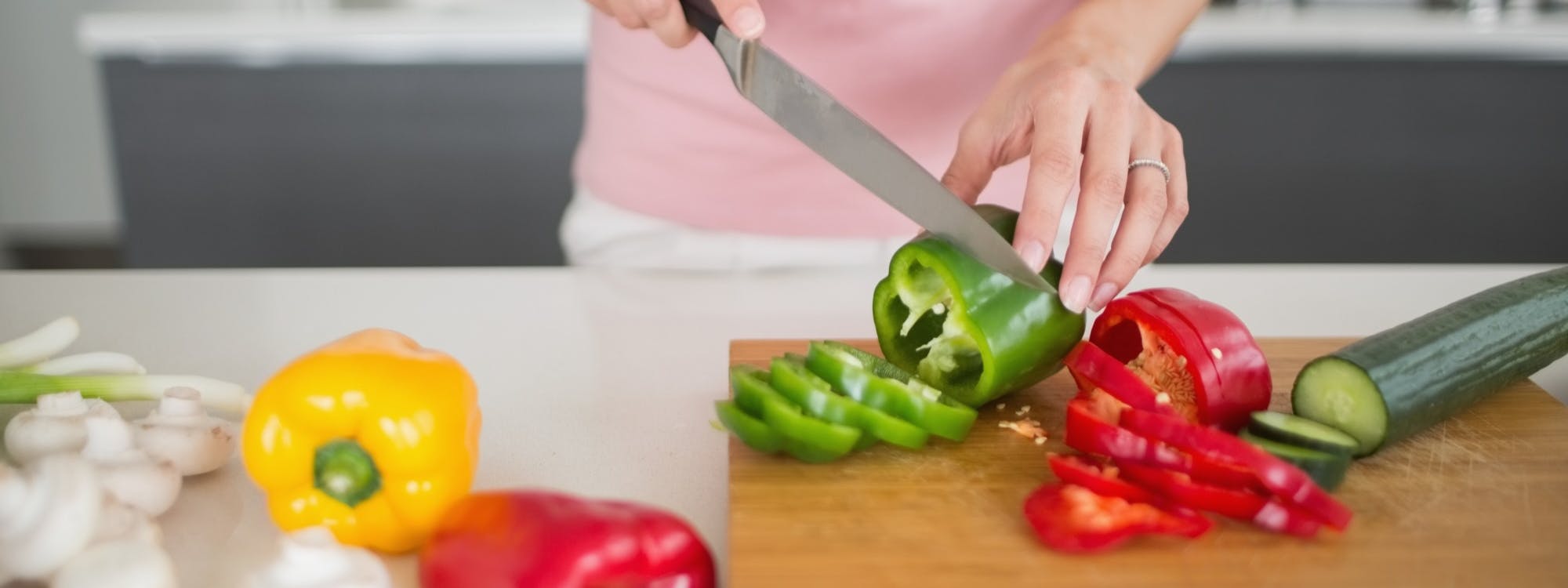 Frau schneidet Paprika und Gurke auf einem Holzbrett Frau schneidet Paprika und Gurke auf einem Holzbrett