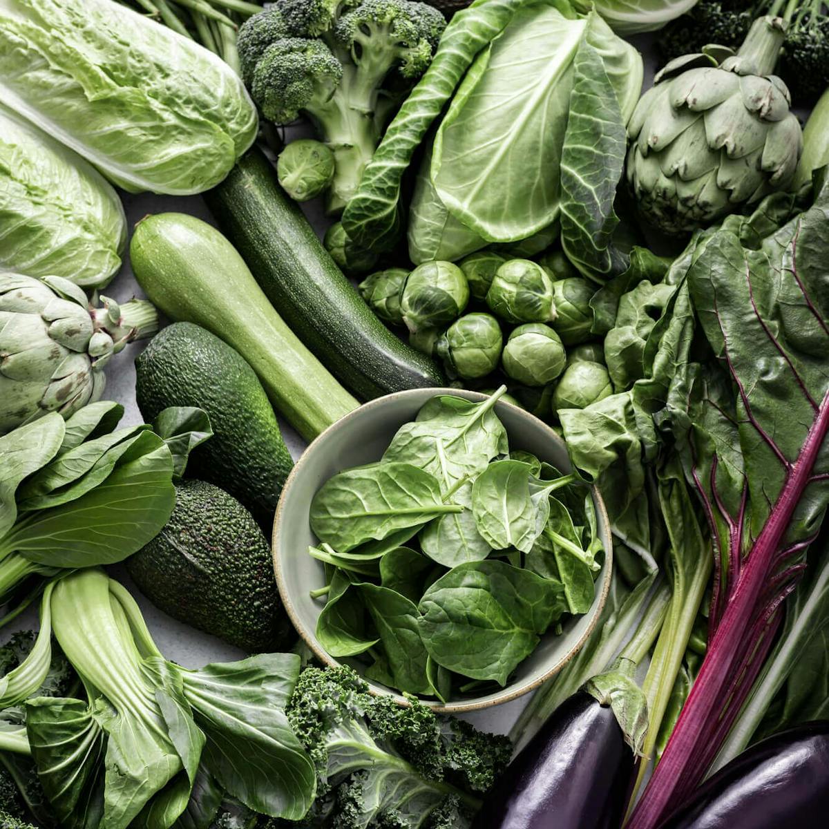 Verschiedenes grünes Gemüse wie Kohl, Brokkoli, Spinat und Avocados liegen nebeneinander auf dem Tisch