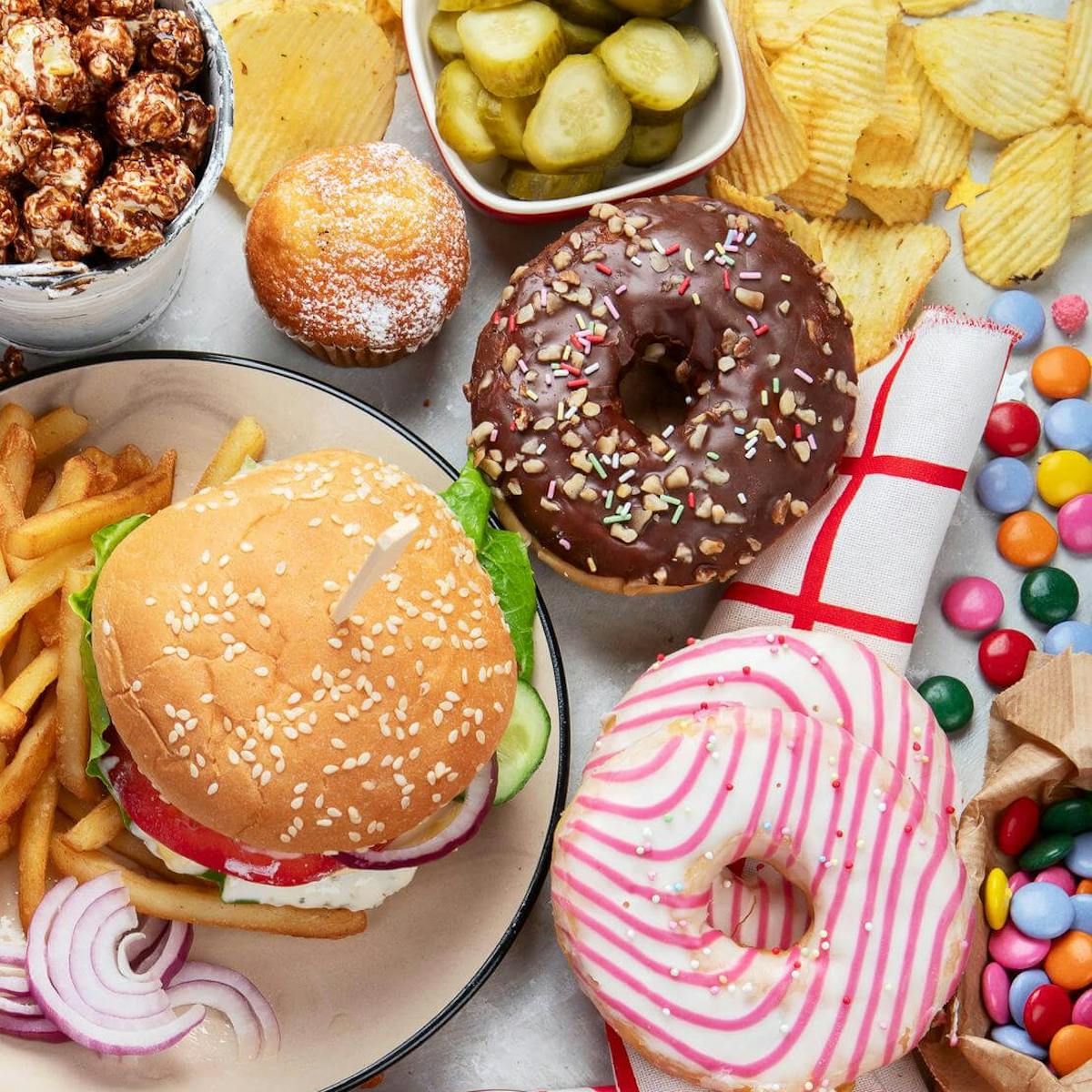 Ungesunde Lebensmittel wie Burger, Donuts, Chips und Süßigkeiten liegen nebeneinander auf einem Tisch