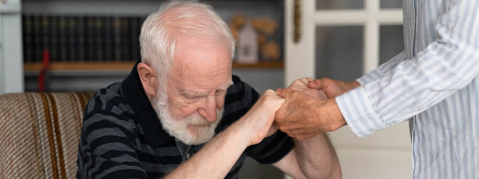 Älterer Mann mit Parkinson bekommt Unterstützung beim Aufstehen aus einem Sessel Älterer Mann mit Parkinson bekommt Unterstützung beim Aufstehen aus einem Sessel