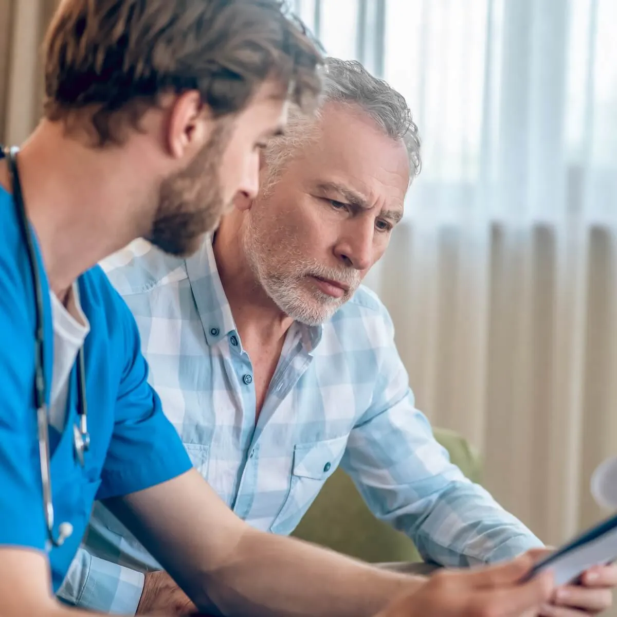 Arzt erklärt männlichem Patienten etwas und hält dabei ein Klemmbrett in der Hand
