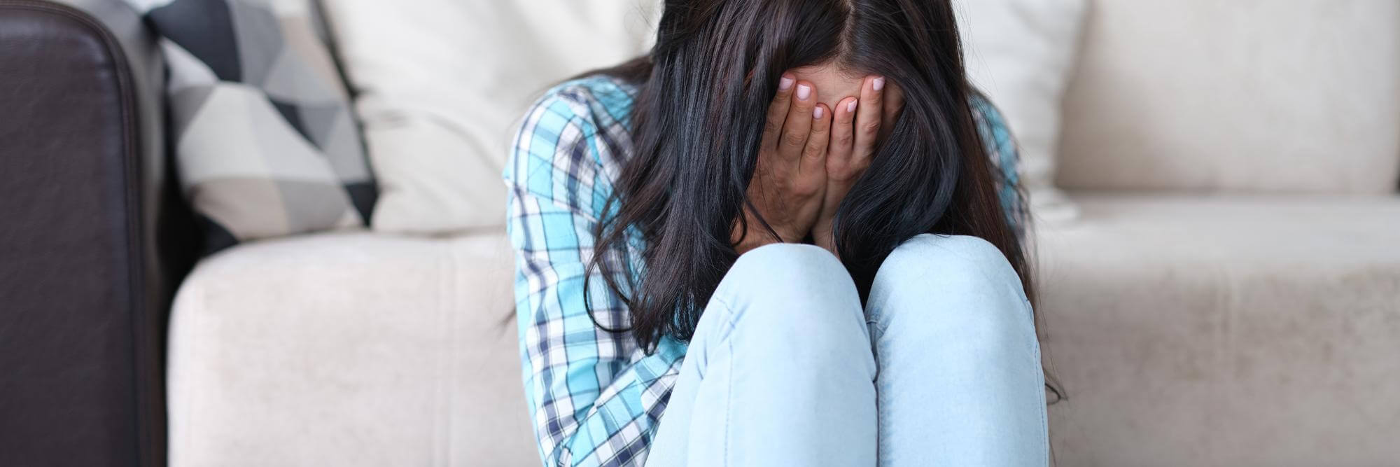 Frau sitzt vor einem Sofa und hält ihr Gesicht in ihre Hände