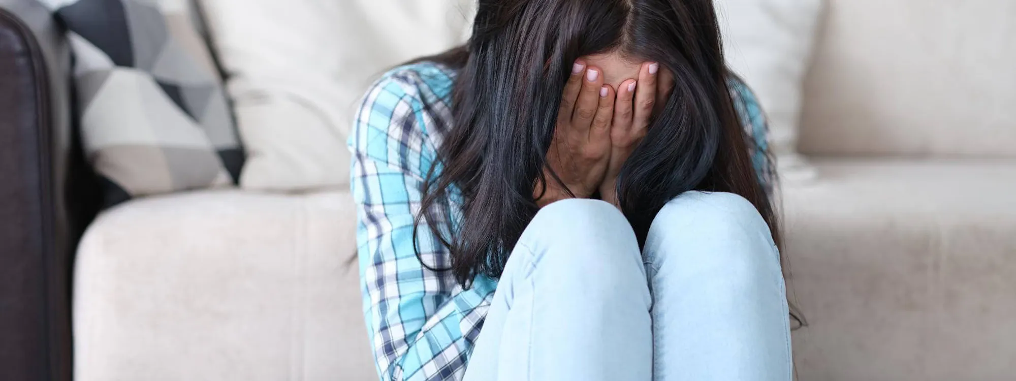 Frau sitzt vor einem Sofa und hält ihr Gesicht in ihre Hände