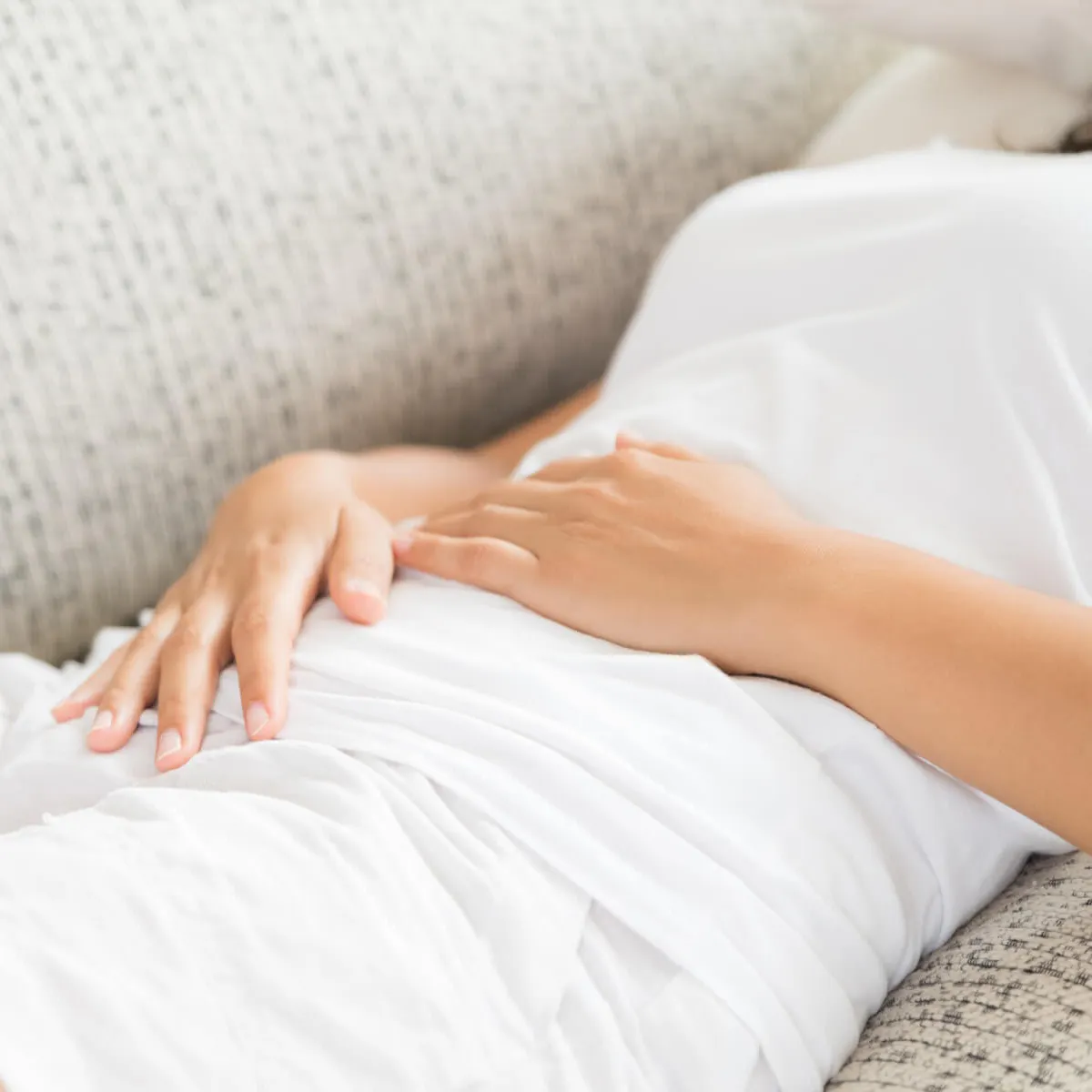 Frau liegt mit Bauchschmerzen auf dem Sofa und hält die Hände auf den Bauch