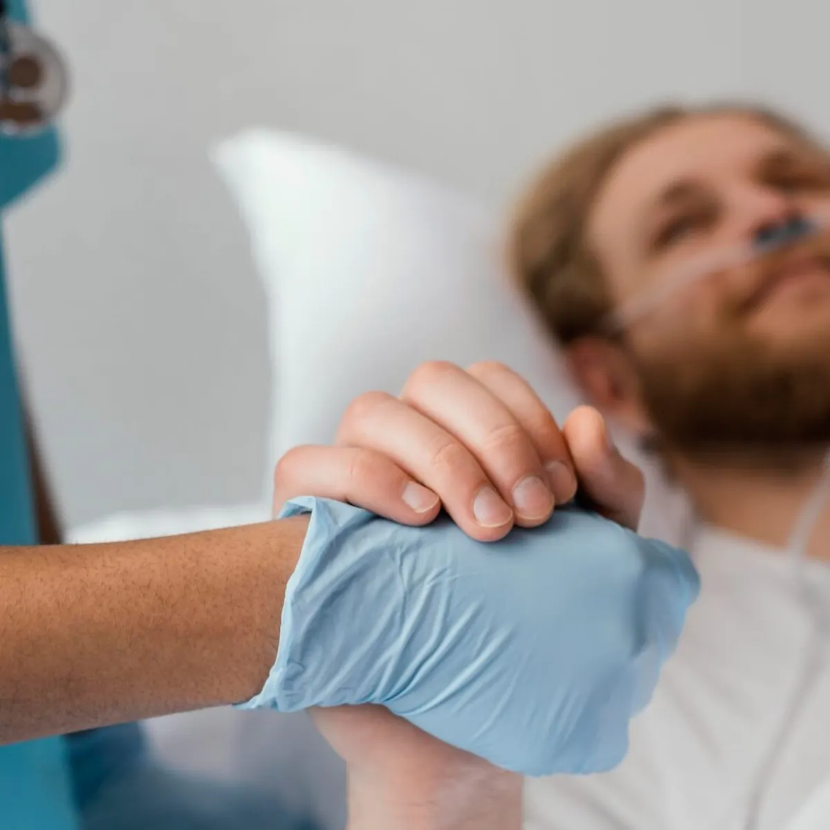 Pflegerin hält die Hand eines männlichen Patienten am Krankenhausbett