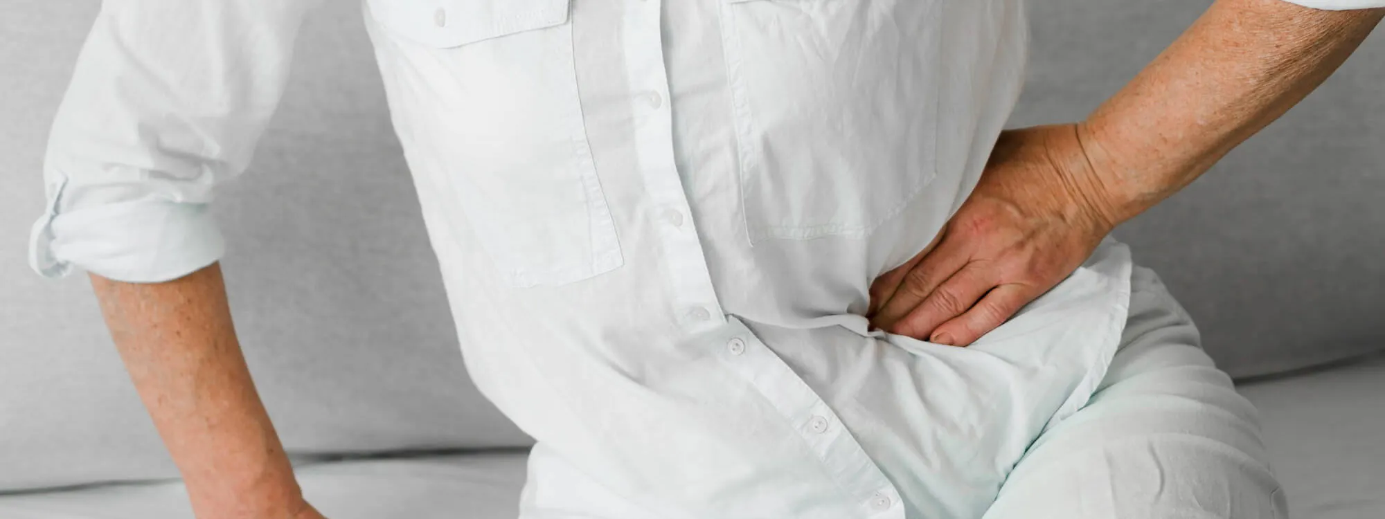 Frau sitzt auf einem Sofa und hält ihre Hand an den seitlichen Bauchraum