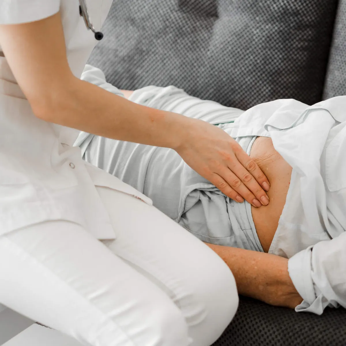 Ärztin tastet den Bauch einer auf dem Sofa liegenden Patientin ab