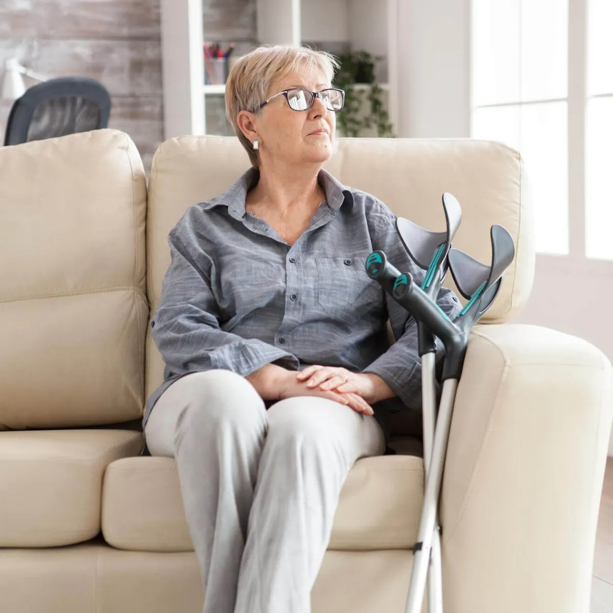 Ältere Frau sitzt auf dem Sofa, neben ihr sind Krücken an das Sofa gelehnt