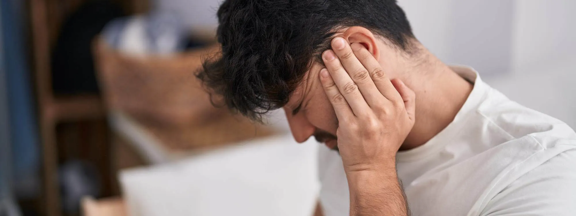 Mann mit chronischem Tinnitus hält sich mit schmerzverzerrtem Gesicht eine Hand ans Ohr Mann mit chronischem Tinnitus hält sich mit schmerzverzerrtem Gesicht eine Hand ans Ohr