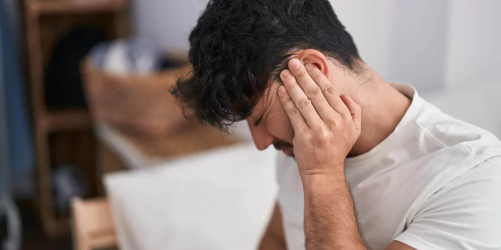 Mann mit chronischem Tinnitus hält sich mit schmerzverzerrtem Gesicht eine Hand ans Ohr Mann mit chronischem Tinnitus hält sich mit schmerzverzerrtem Gesicht eine Hand ans Ohr