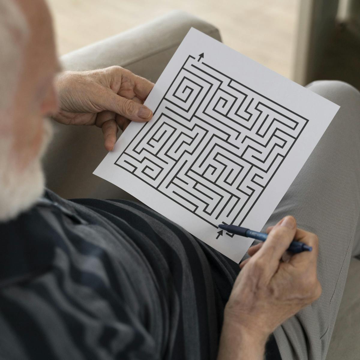 Älterer Mann sitzt und löst ein Rätsel Labyrinth mit einem Stift