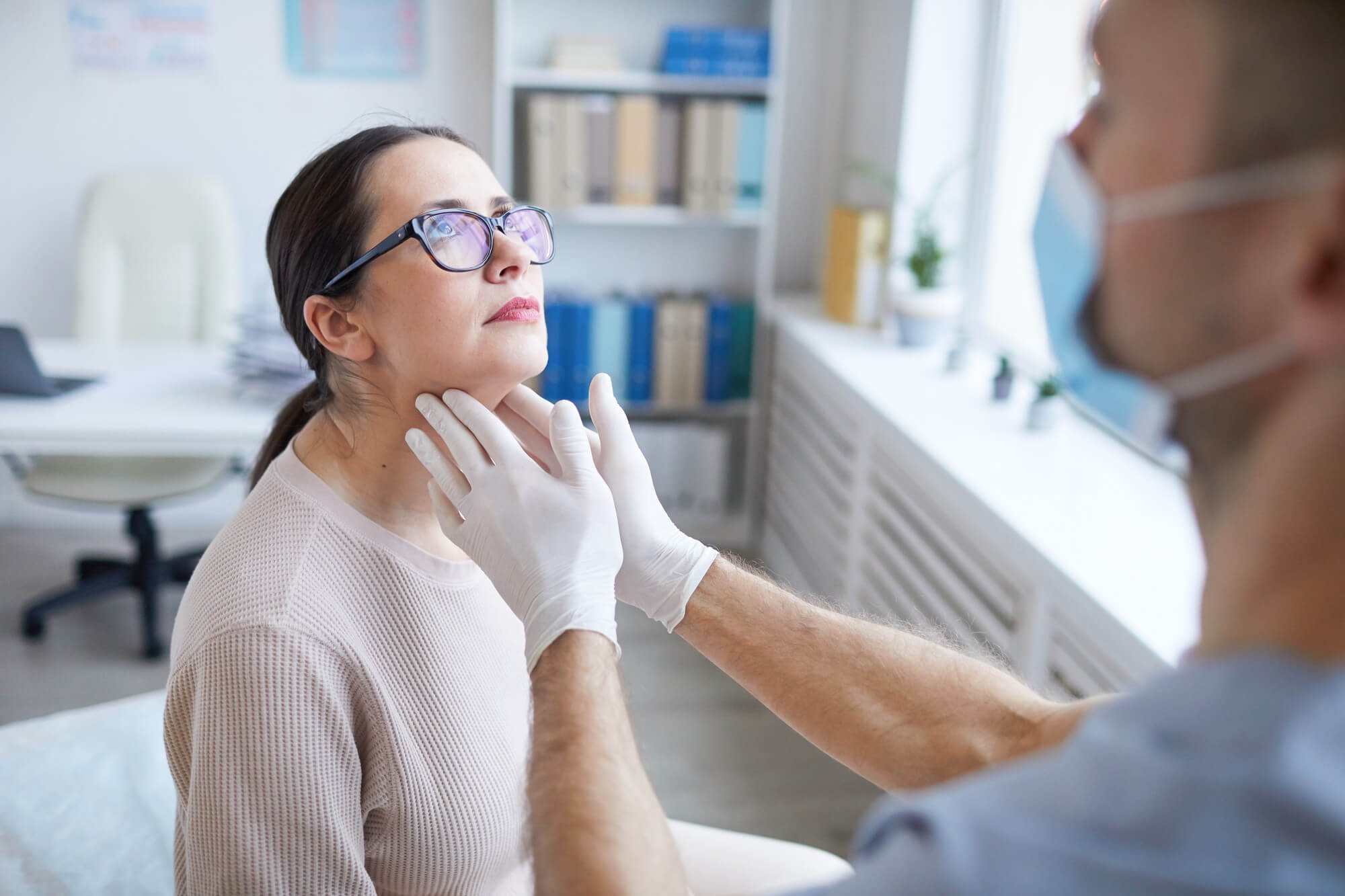Arzt tastet den Hals einer Patientin ab