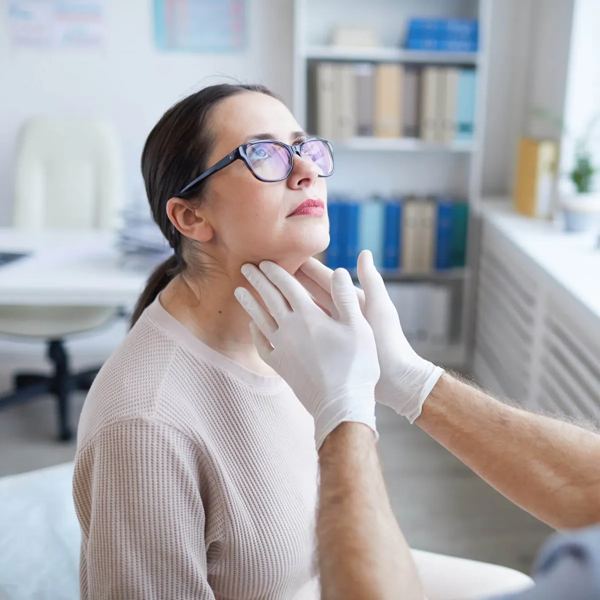Weibliche Patientin wird von einem Arzt am Hals untersucht