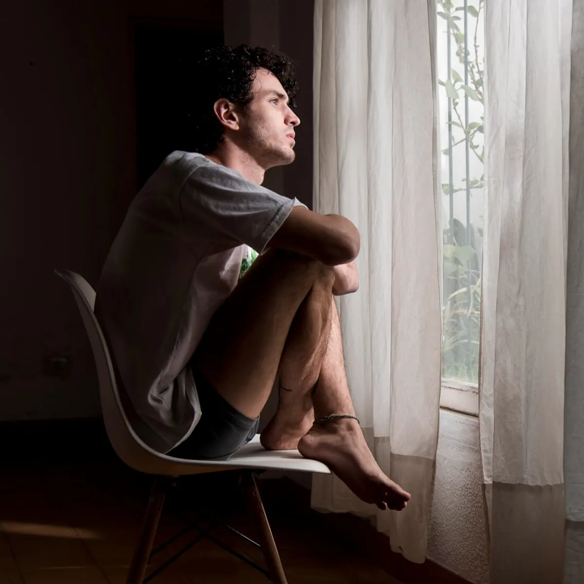 Mann sitzt auf einem Stuhl und schaut traurig aus dem Fenster