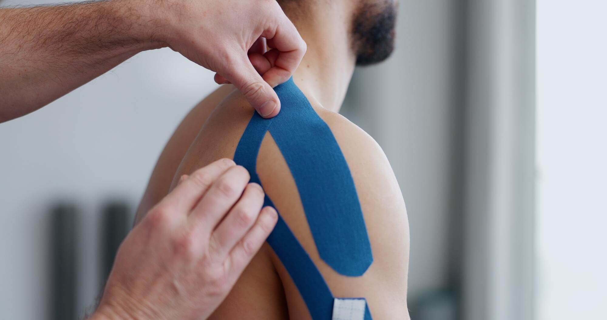 Physiotherapeut klebt einem Mann blaues Tape auf die Schulter