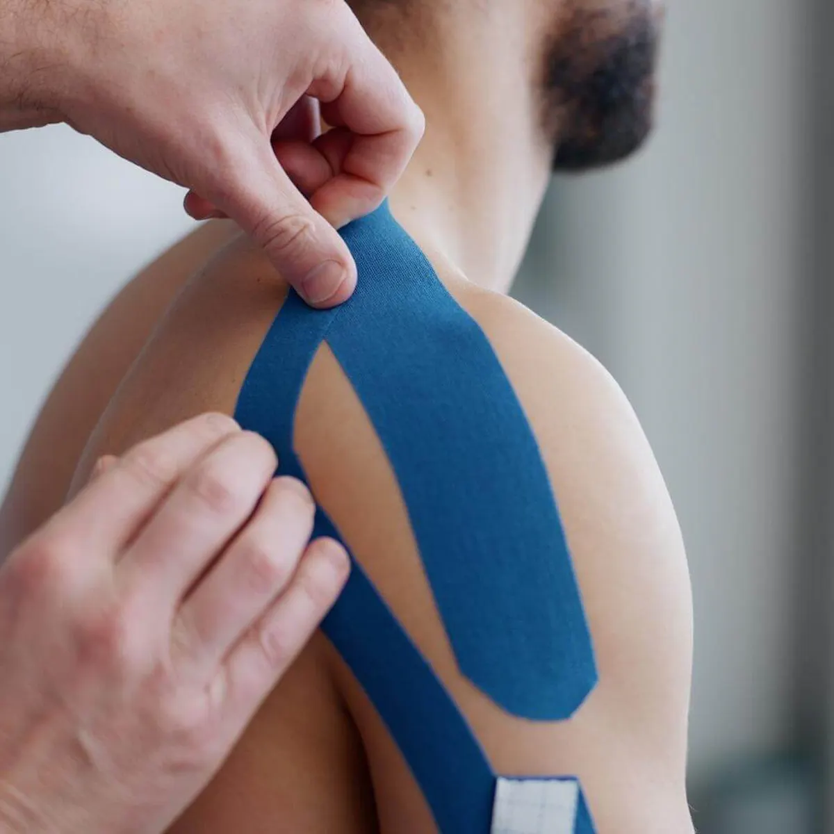 Physiotherapeut klebt einem Mann blaues Tape auf die Schulter