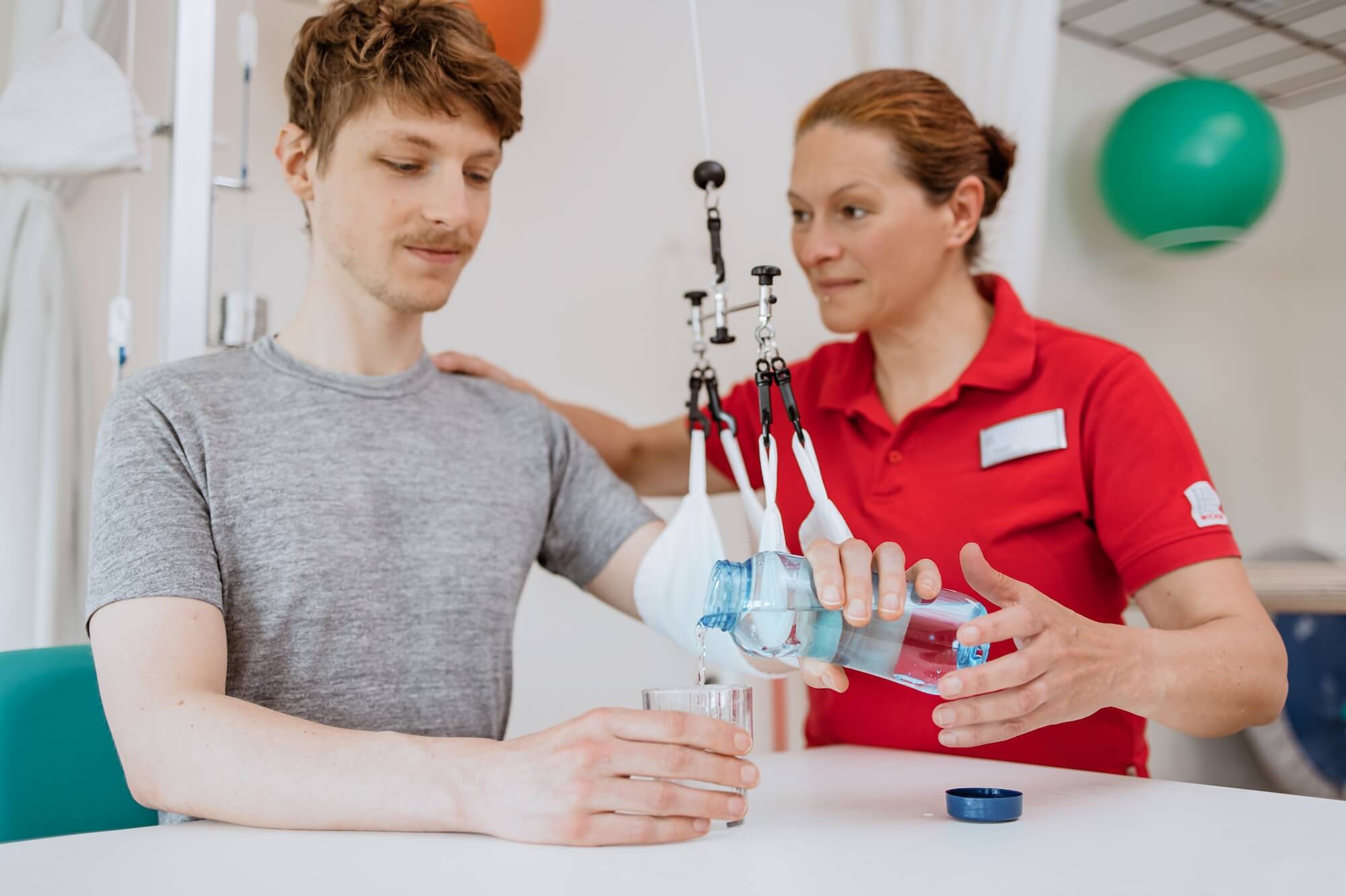 Therapeutin übt mit einem Patienten Wasser einschenken