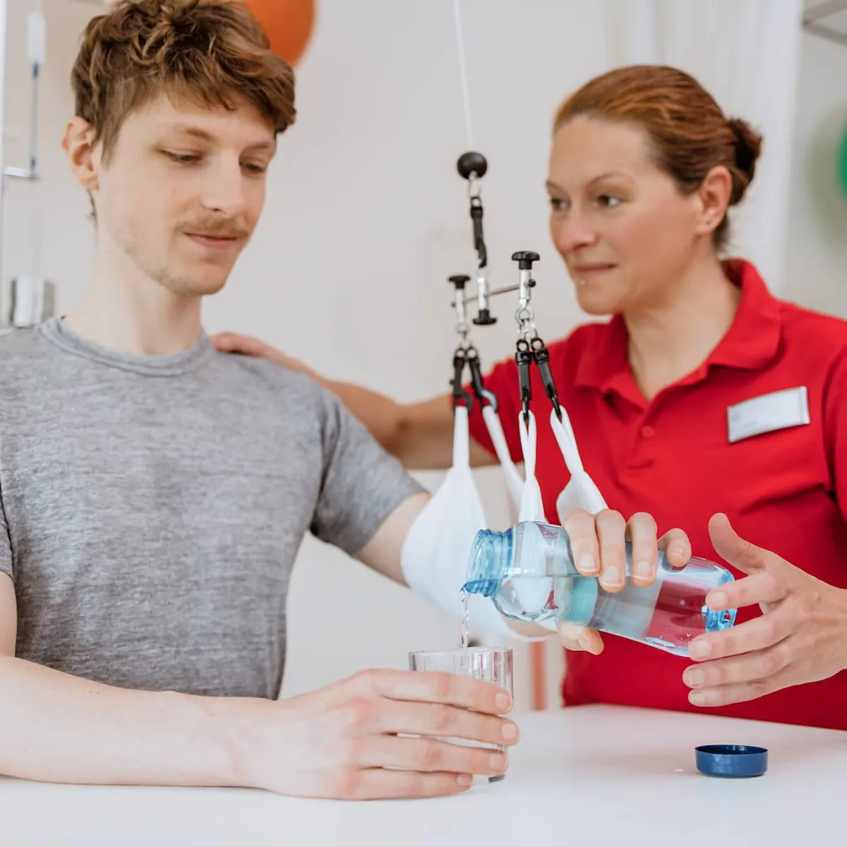 Therapeutin übt mit einem Patienten Wasser einschenken