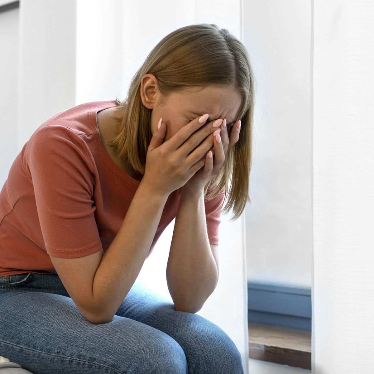 Junge Frau sitzt mit gesenktem Kopf und verbirgt ihr Gesicht in den Händen