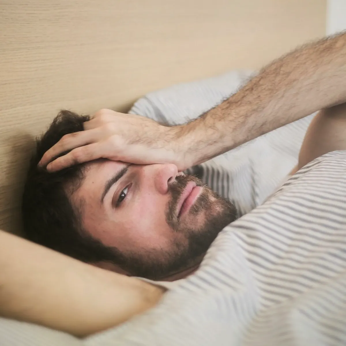 Mann liegt im Bett und hält sich mit schmerzverzogenem Gesicht ein Auge mit der Hand zu
