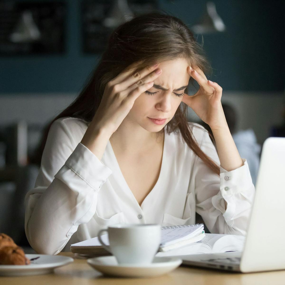 Frau mit Kopfschmerzen sitzt vor ihrem Laptop und fasst sich an die Stirn