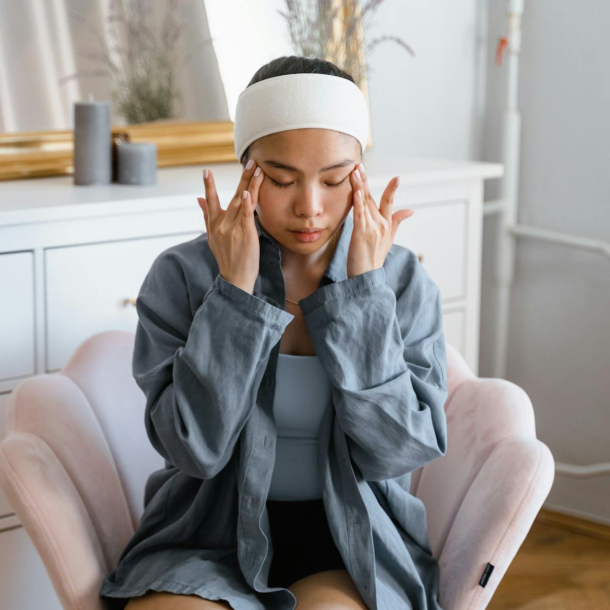 Junge Frau sitzt auf einem Sessel und fasst sich die Schläfen