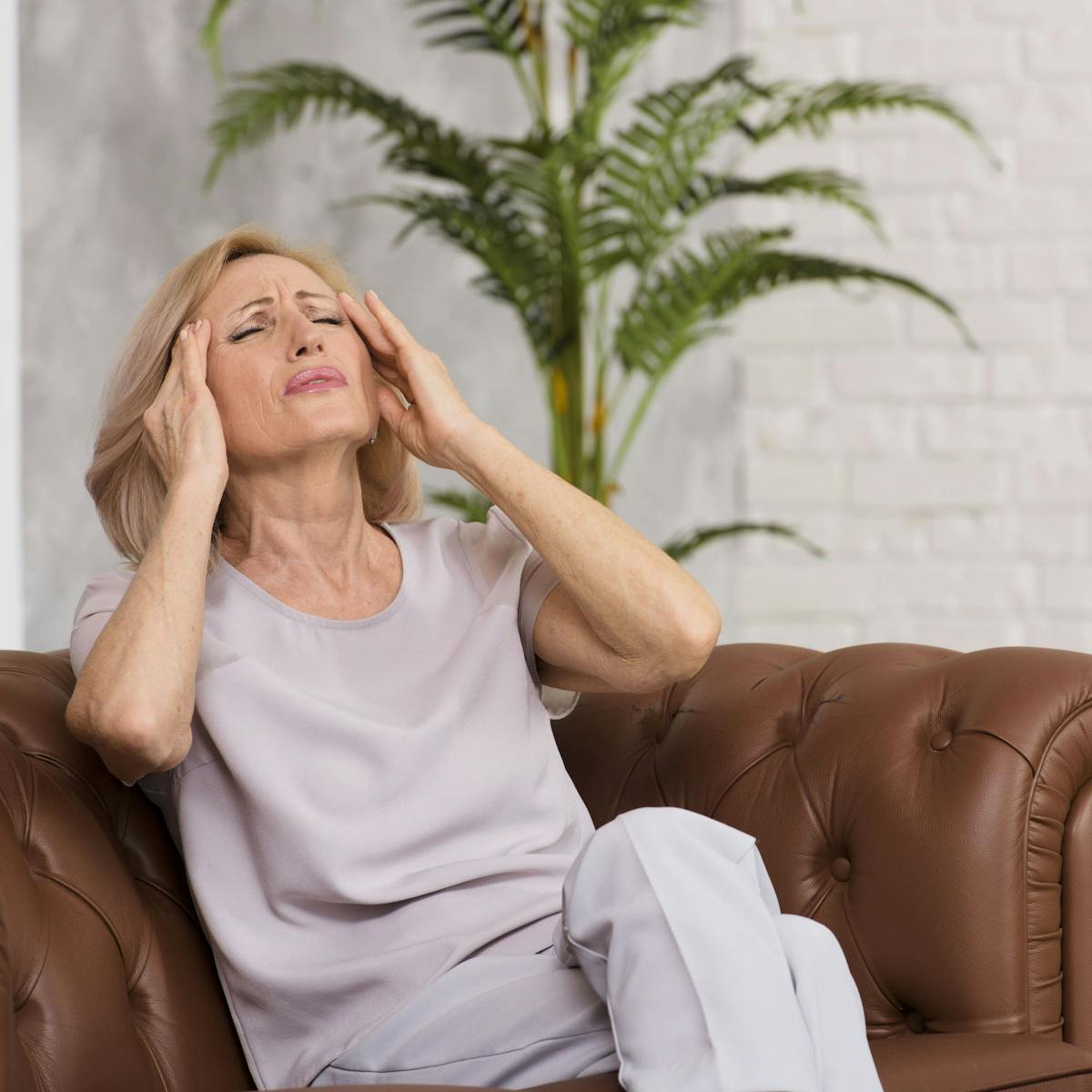 Frau mit schmerzverzogenem Gesicht sitzt auf dem Sofa und fasst sich an den Kopf