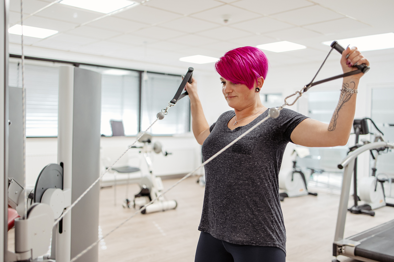 Patientin macht eine Kraftübung am Gerät bei der Physiotherapie
