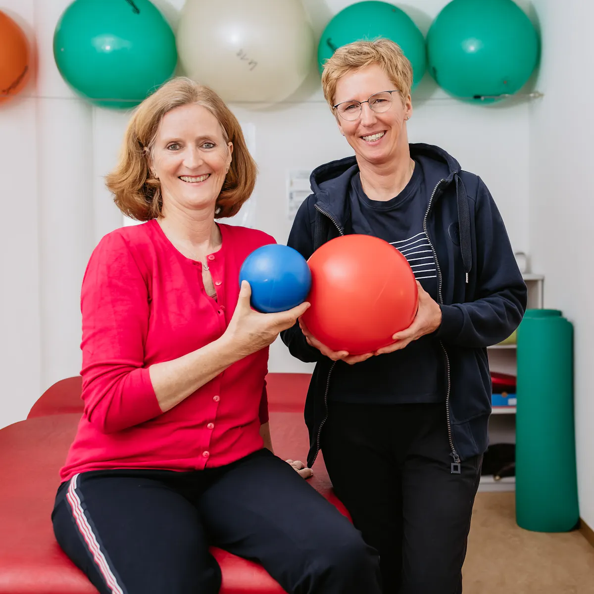 Patientin und Physiotherapeutin stehen nebeneinander und halten Bälle in der Hand