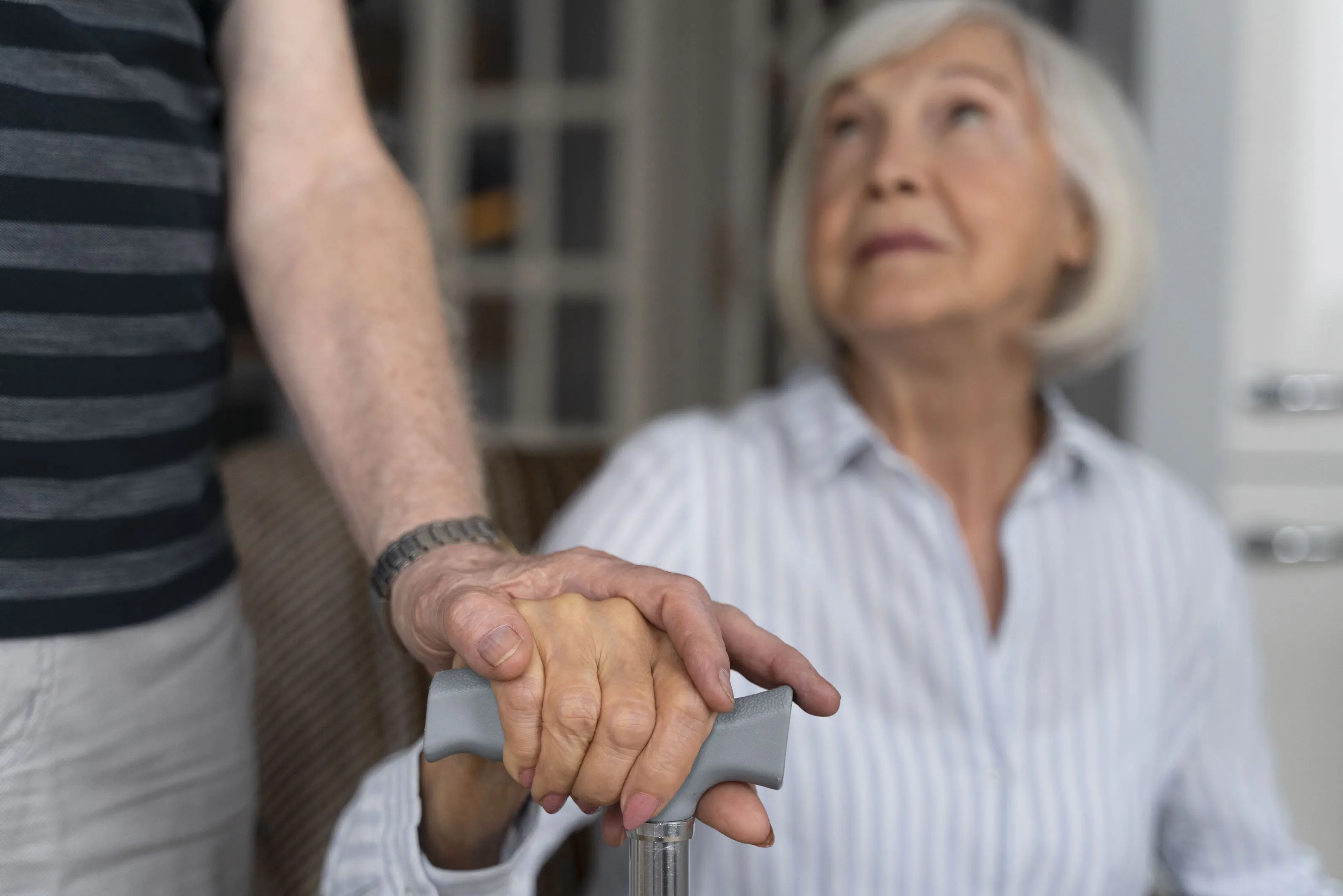 Mann hält die Hand einer älteren Frau am Gehstock