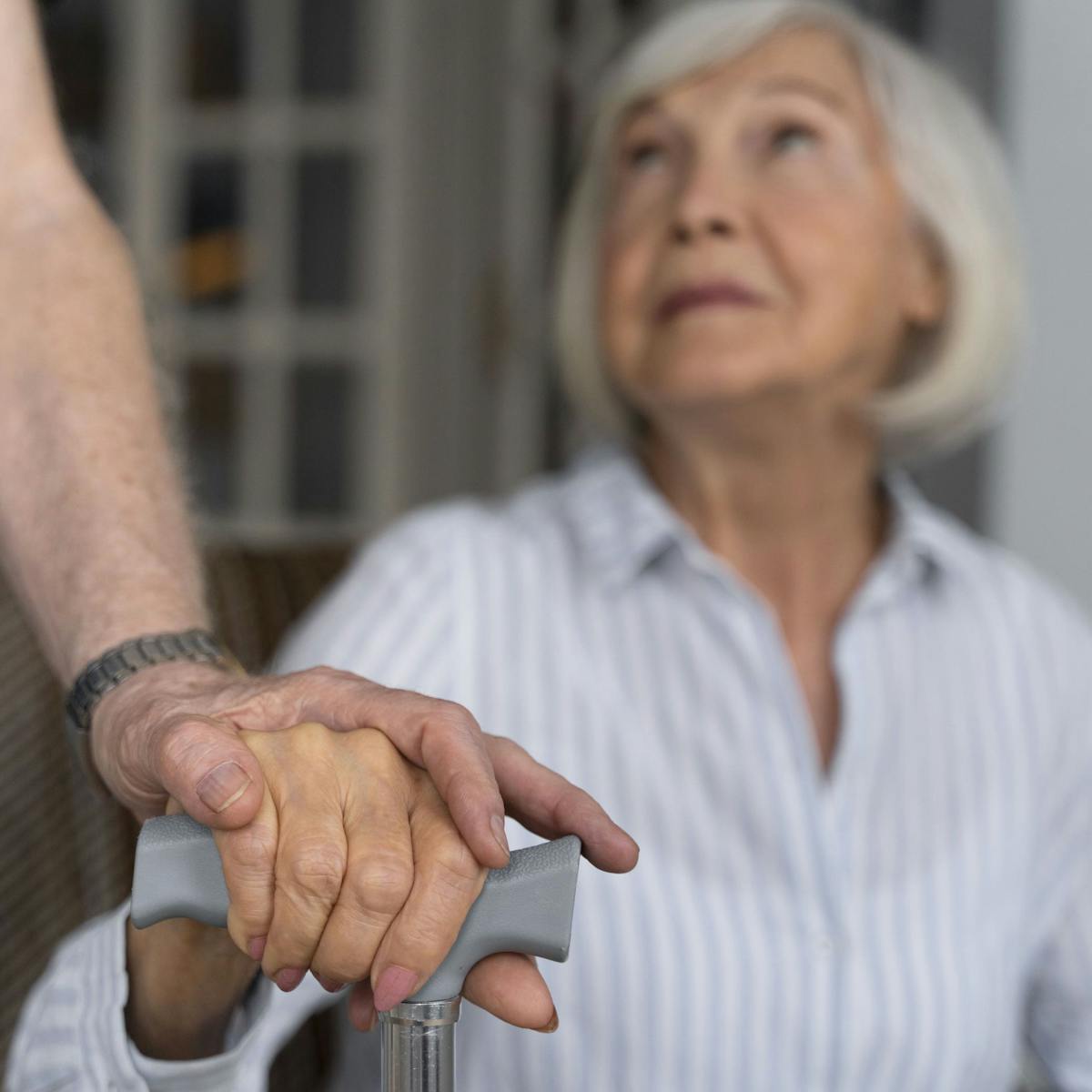 Ältere Frau mit Parkinson hält sich an Gehhilfe fest und schaut andere Person an