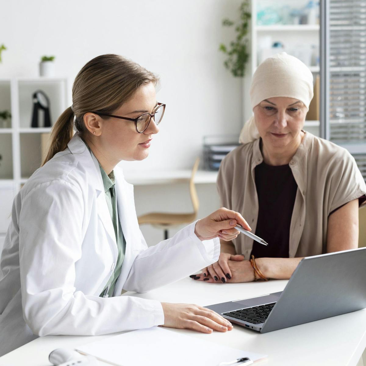 Ärztin zeigt mit Stift auf einen Laptop und erklärt Krebspatientin etwas
