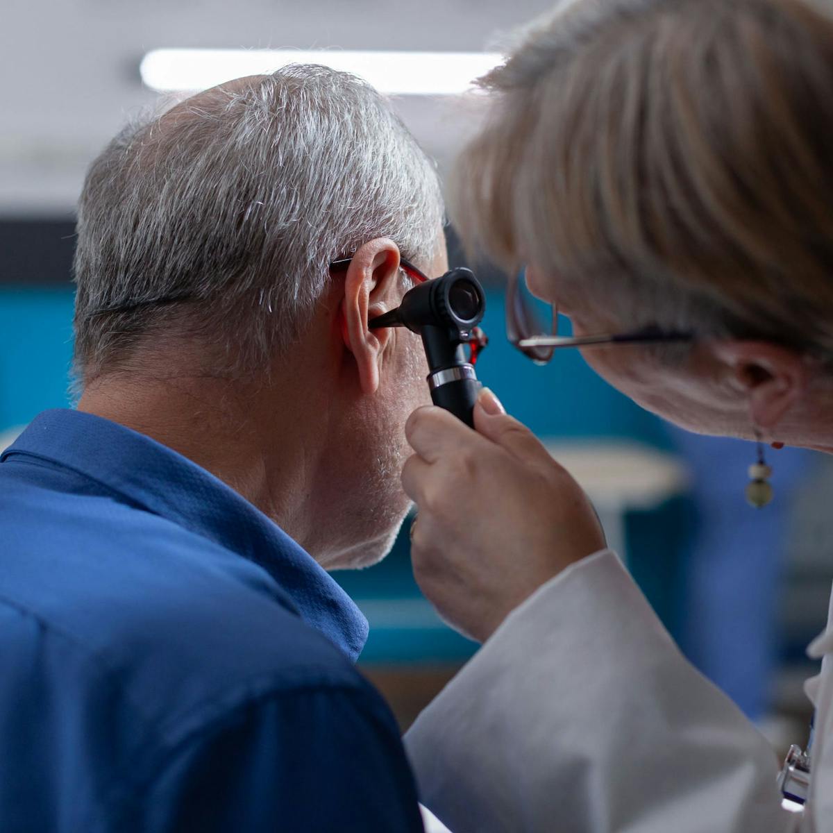Ohr eines Patienten wird von HNO Ärztin untersucht