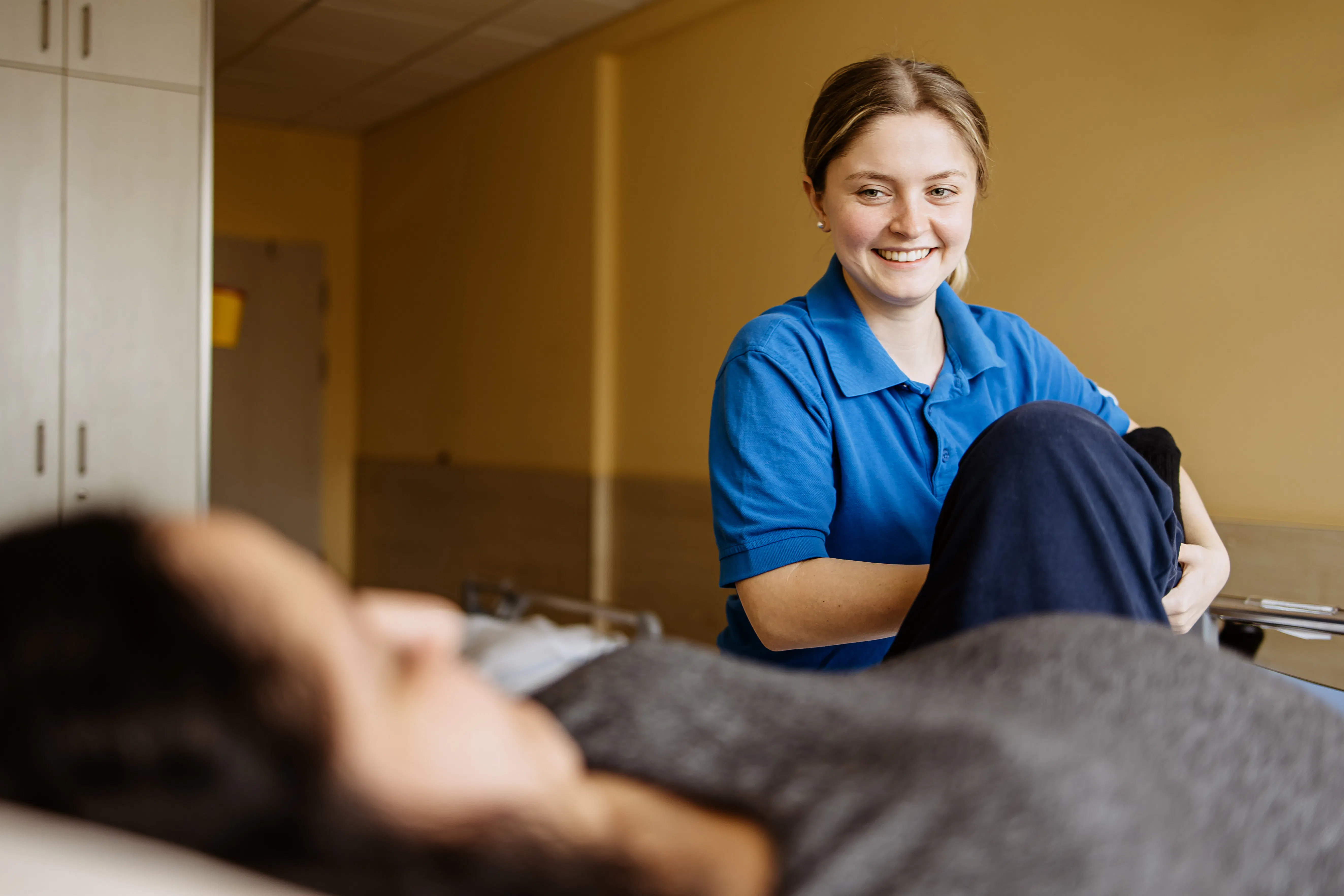 Krankenpflegerin hilft einer Patientin das Bein zu bewegen