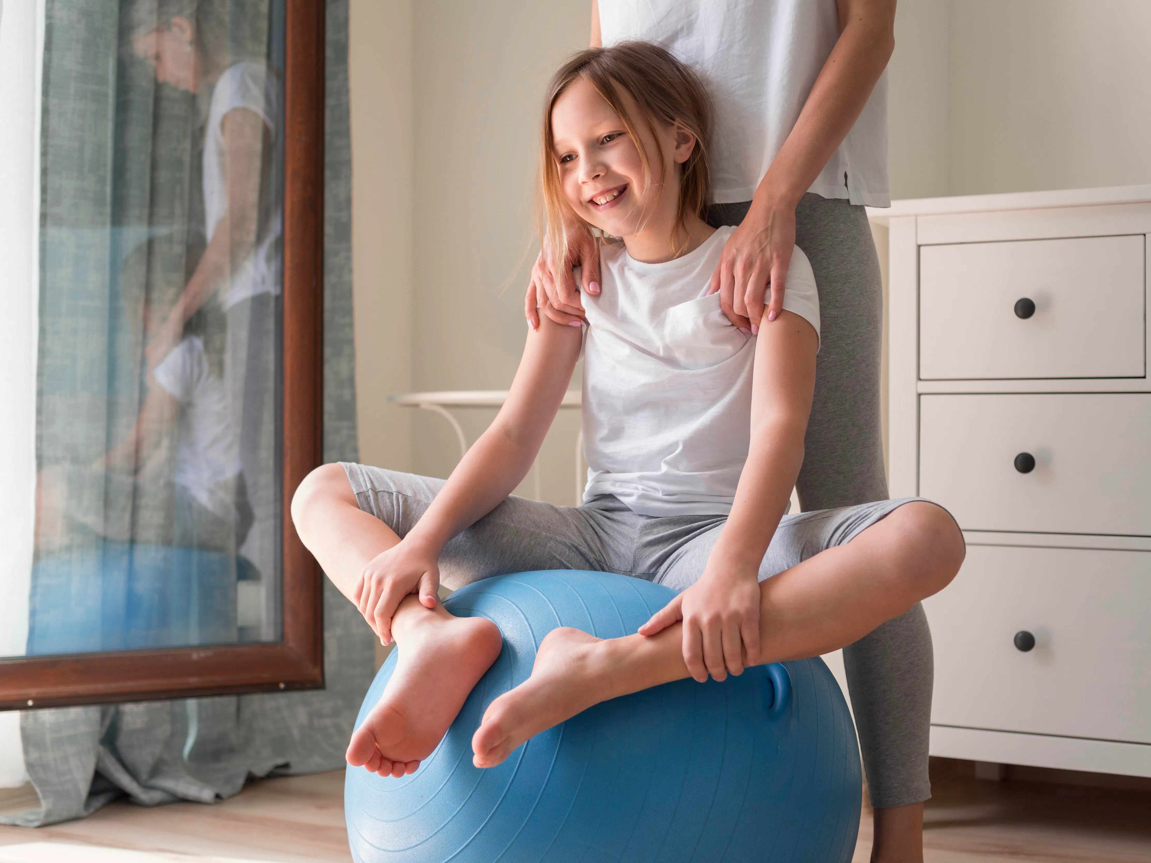 Mädchen sitzt auf Gymnastikball und eine erwachsene Person steht dahinter