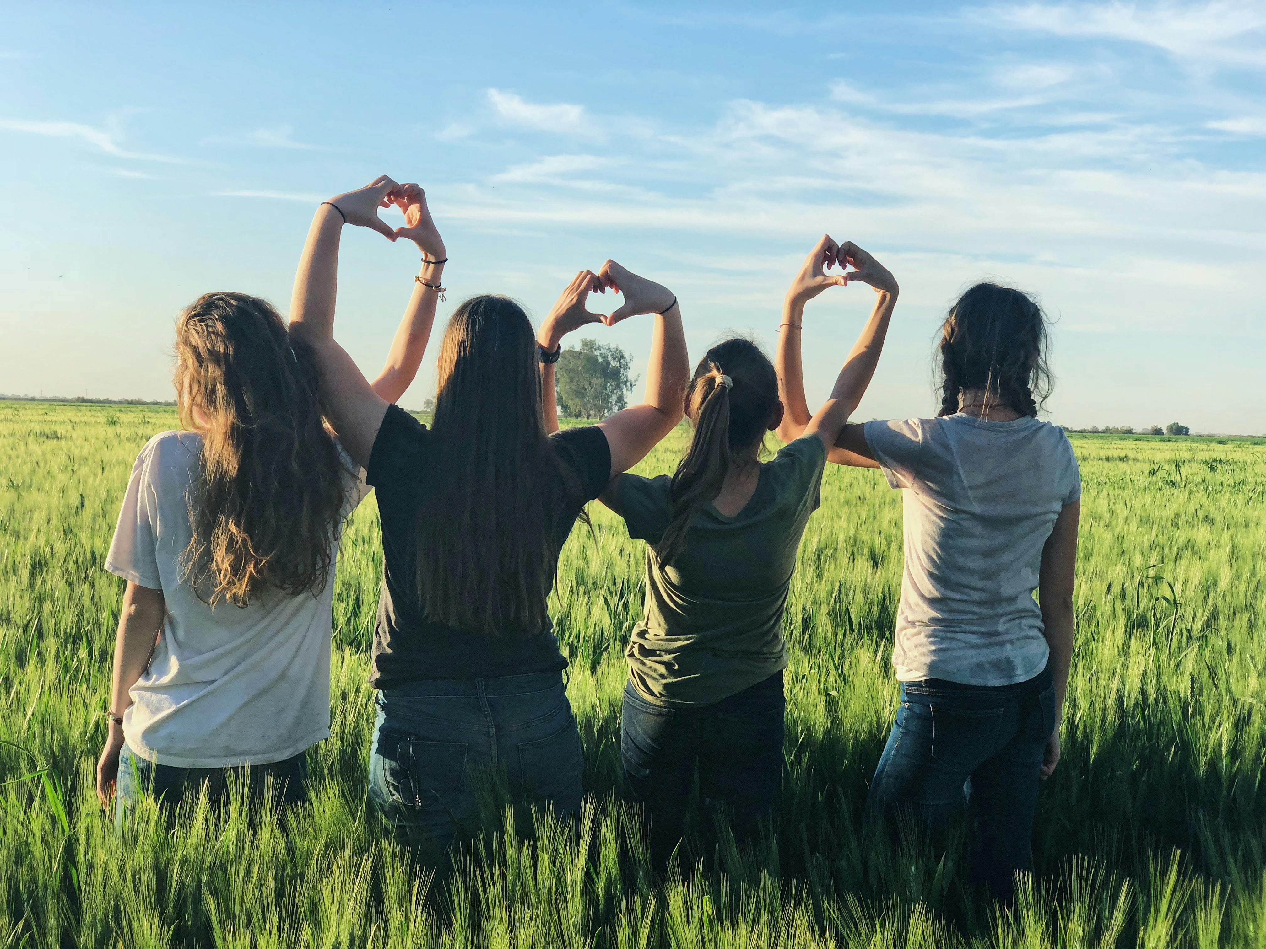 People in grass field making heart symbols with their hands in the air