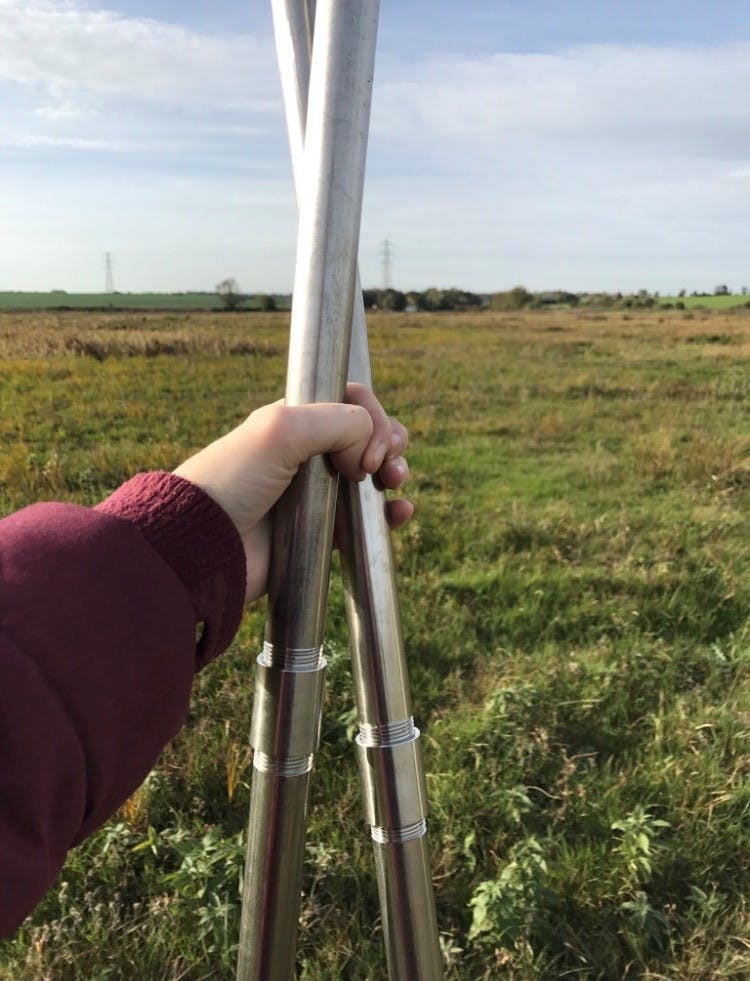 A hand holding two metal poles in front of a grassy field
